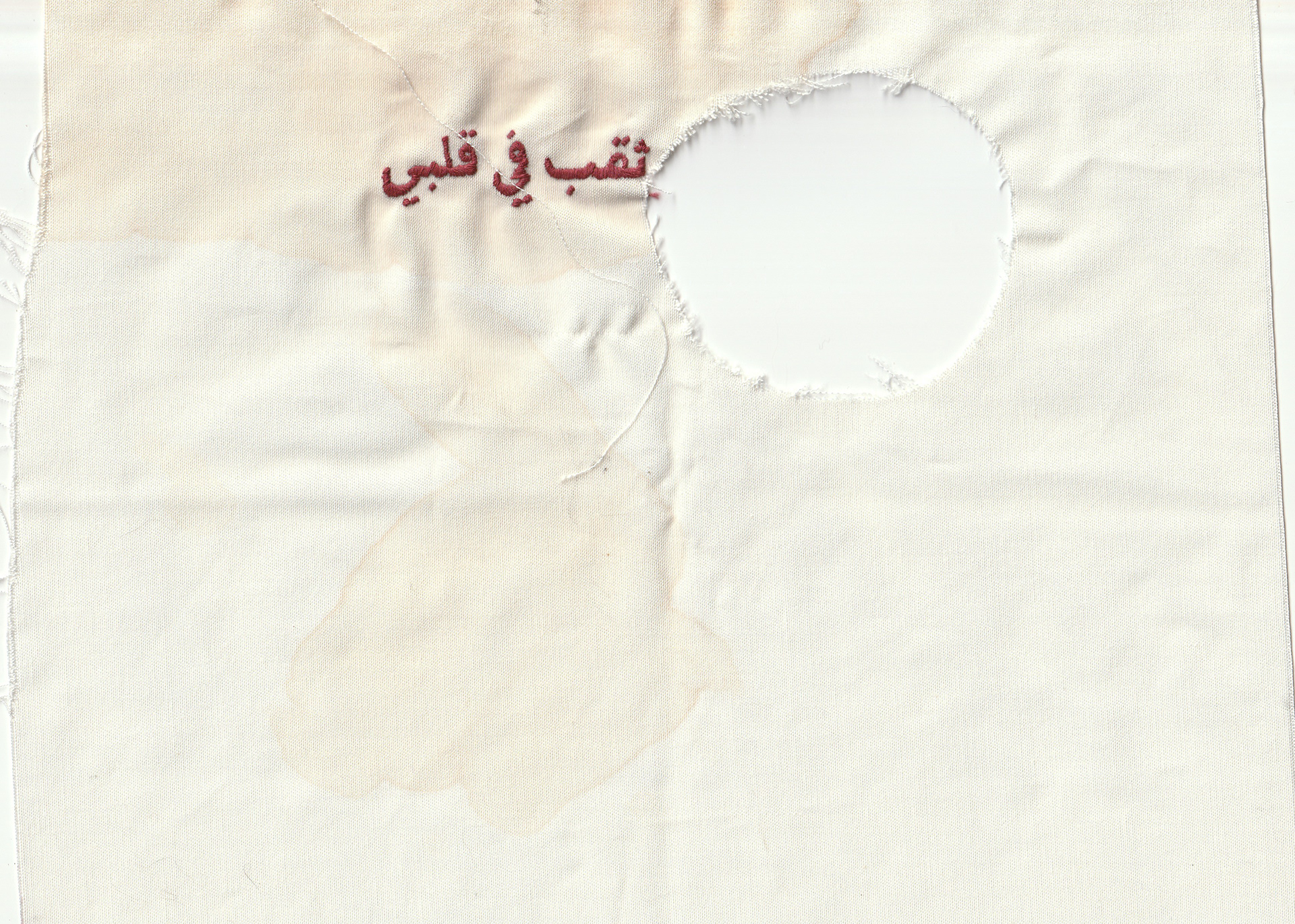 Detail (embroidery) — Text in image (Arabic → English): 'A hole in my heart.' 