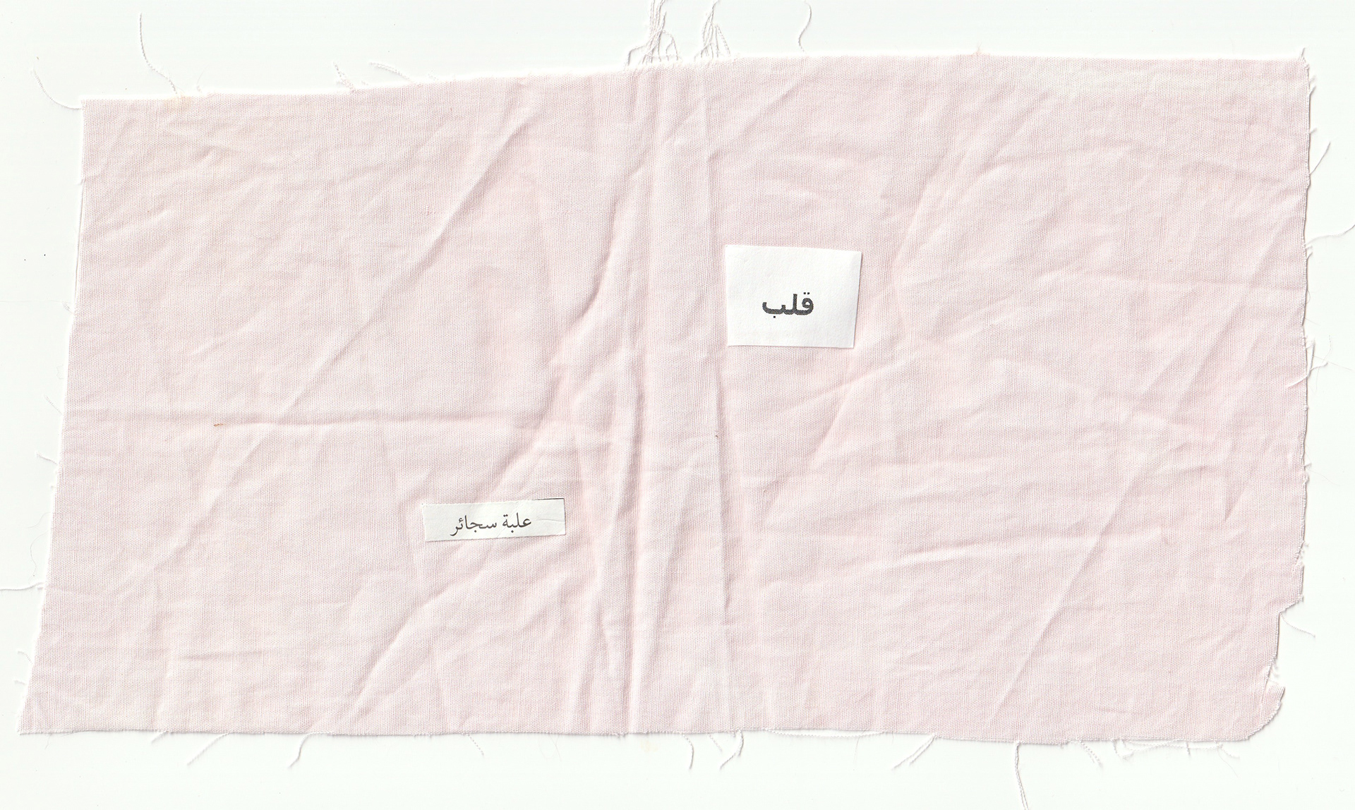 Detail (text collage and fabric) — Text in image (Arabic → English): 'Heart, a cigarette pack.' 