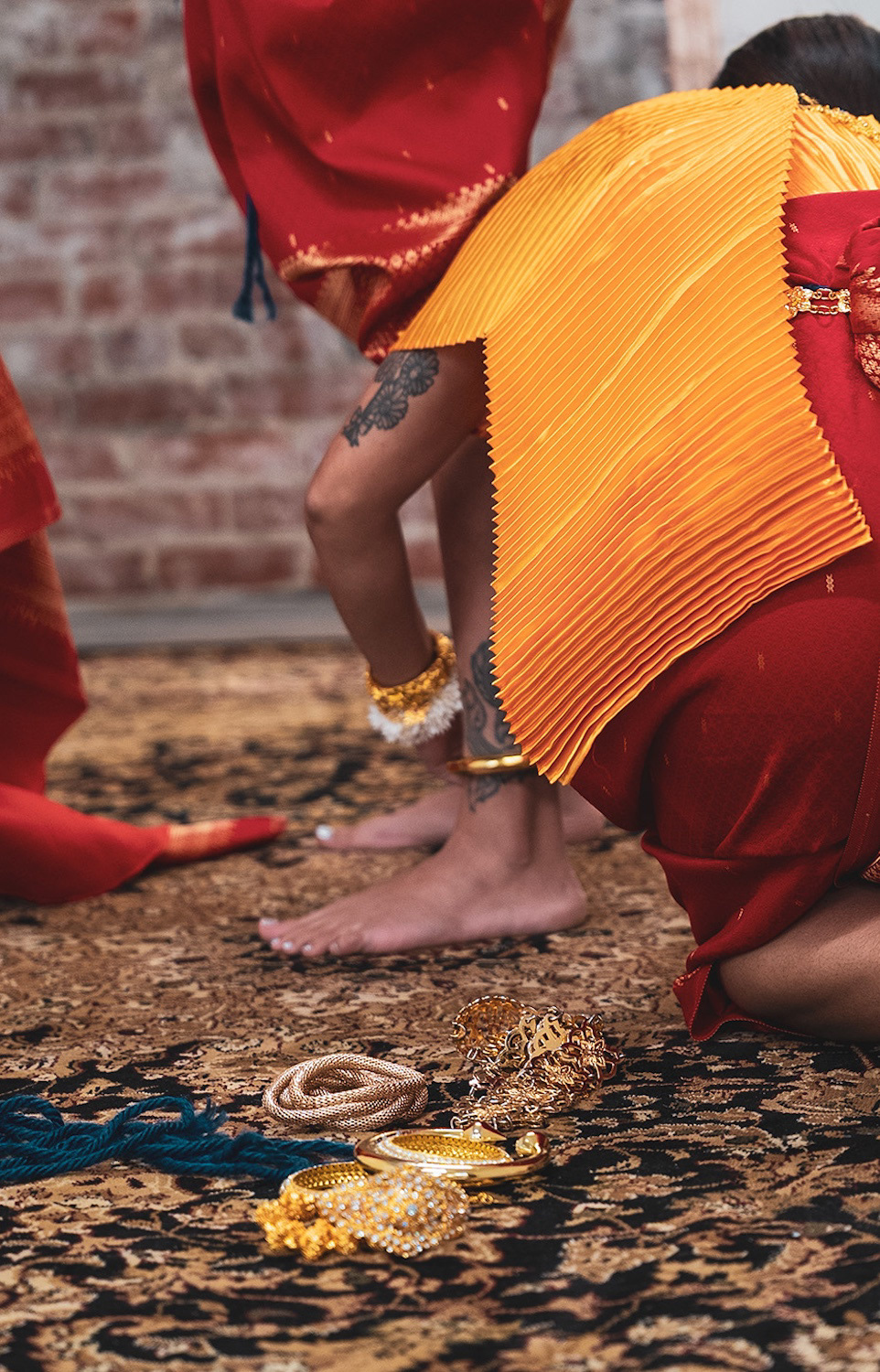 Gold bracelets adorn the dancers. Here, one dancer places an ankle bracelet on another as they continue preparing.
