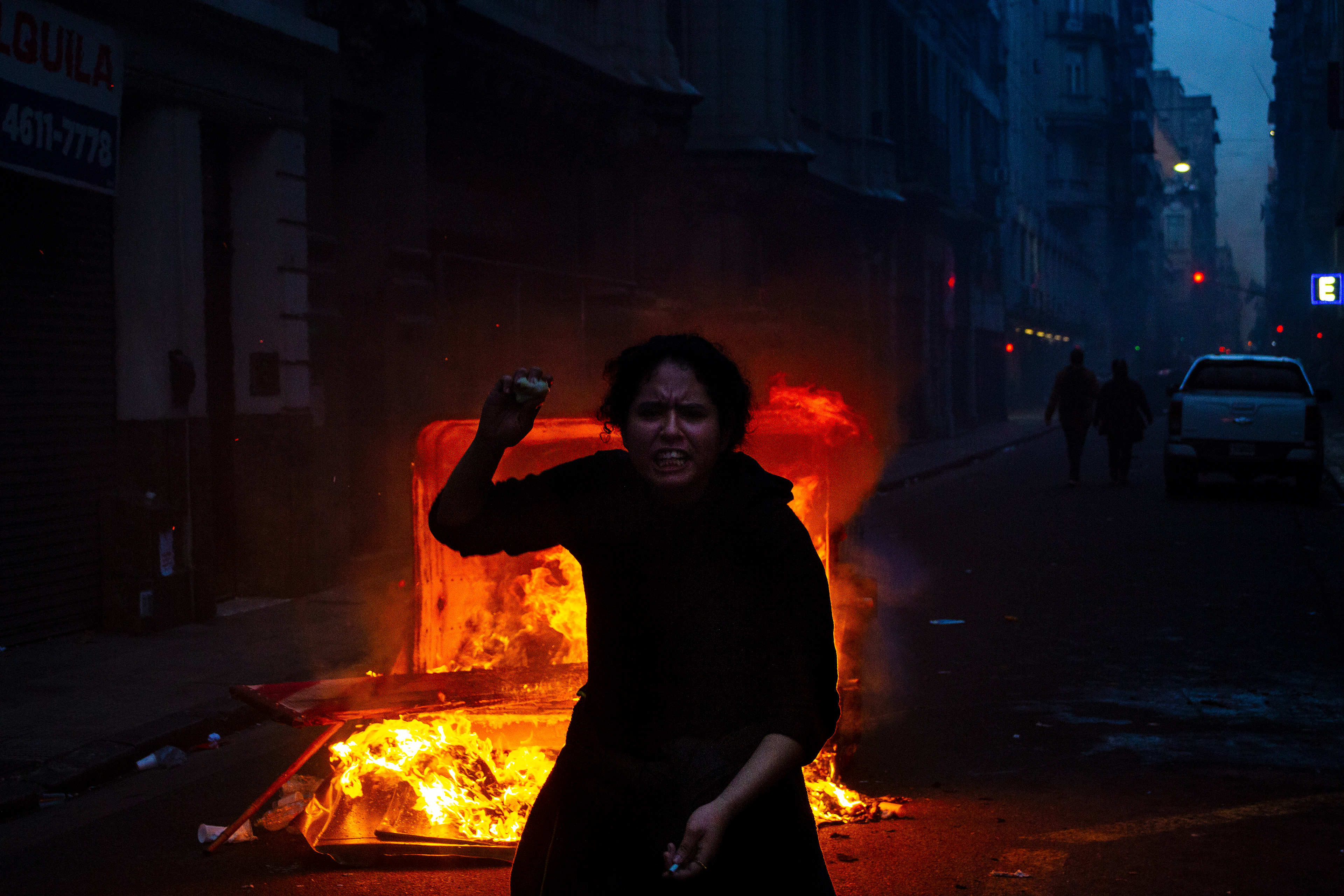 A passerby stands next to a burning trash container during clashes between protestors and security forces outside Congress during the debate of the 'Ley de Bases' reform bill in Buenos Aires, Argentina. June 12, 2024. (Photo by Catriel Gallucci Bordoni) 