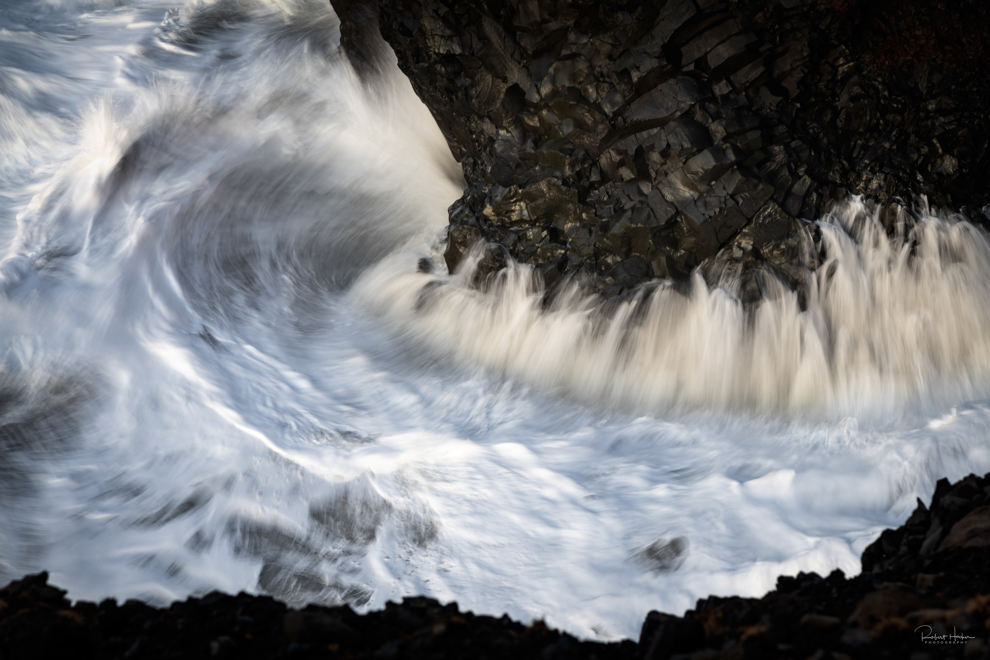 Wave crashing into the basalt cliffs at the Kirkjufjara Beach Overlook