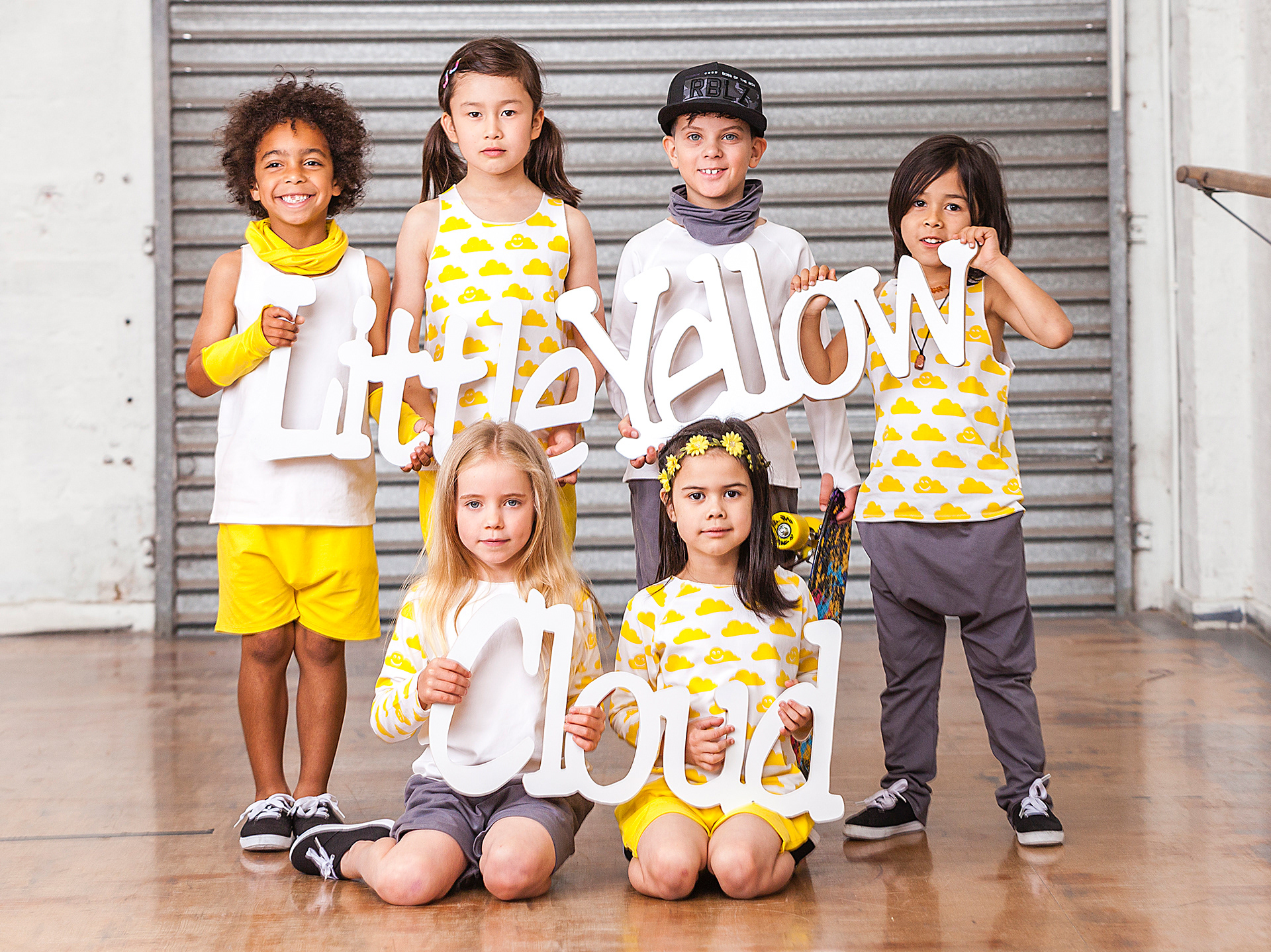 Kids holding up the words Little Yellow Cloud wearing clothing from the range.
