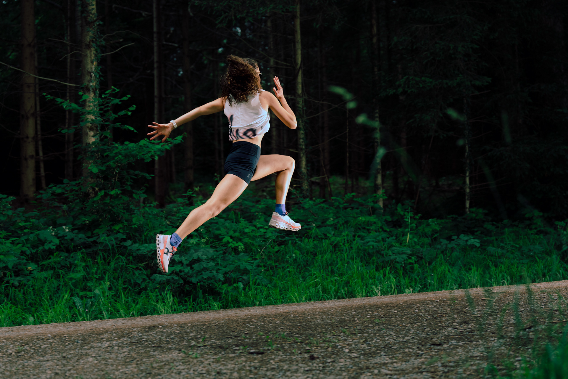 A female Runner trains on a dirt path in the forest. The runner is Bounding energetically with height off the trail.