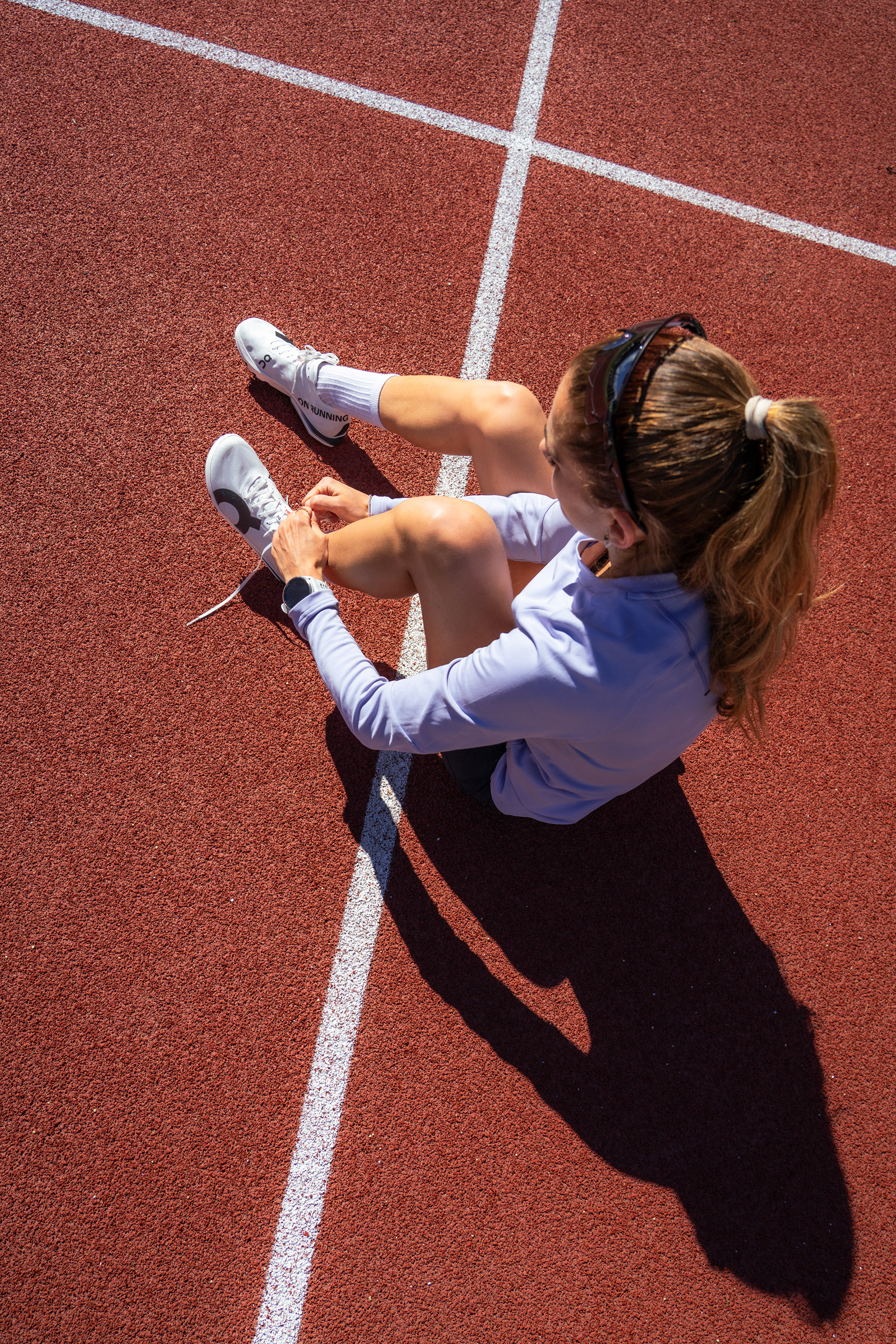 Athlete Marta Garcia. An athlete ties her On Track Spikes whilst sitting on the red track surface.