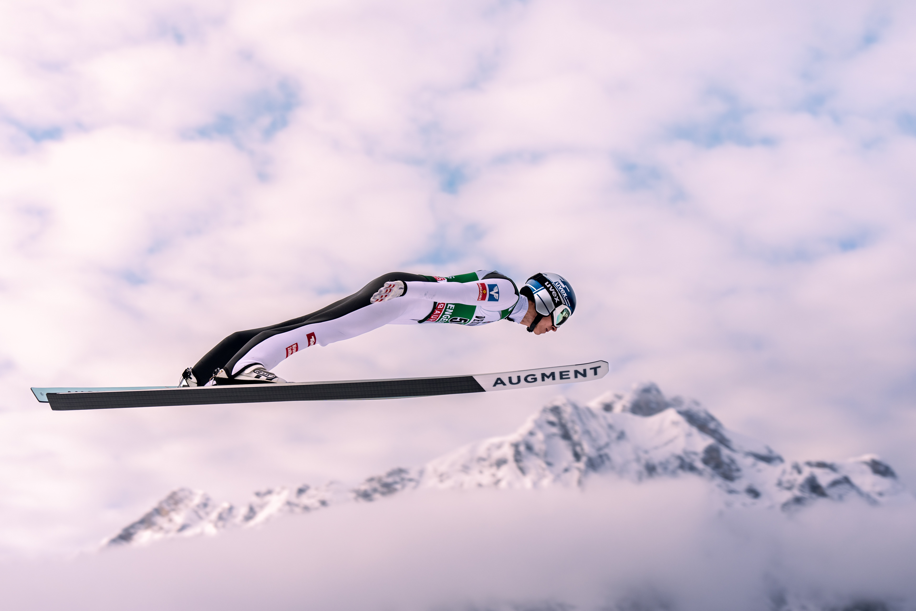 A ski Jumper laying almost flat on his skis flying above the Swiss Alps. Engelberg, Switzerland. Red Bull Athlete. Ski Jumping photographer