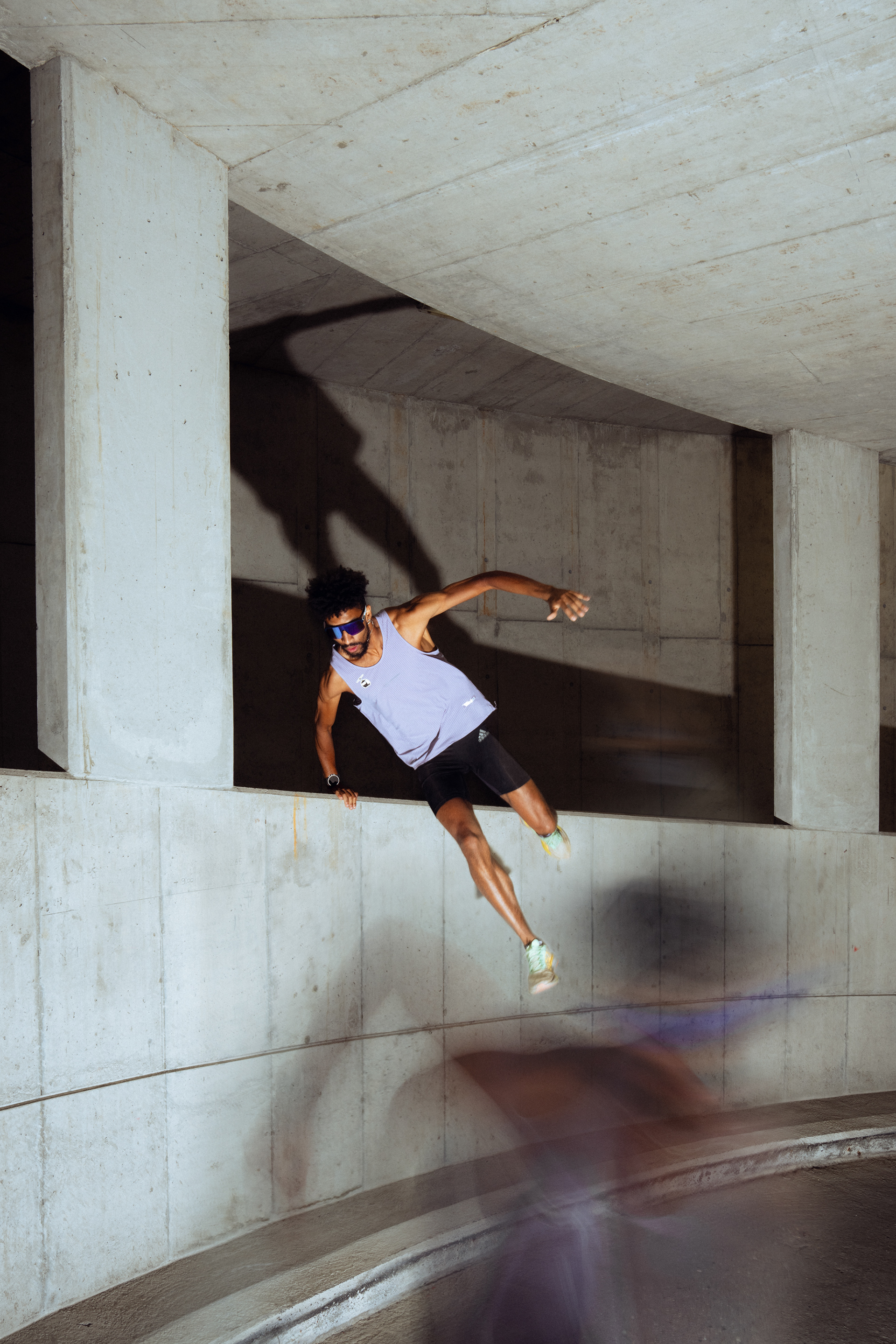 Runner jumping over a wall in a parking garage. The photograph uses motion and flash to juxtapose energy and calm.