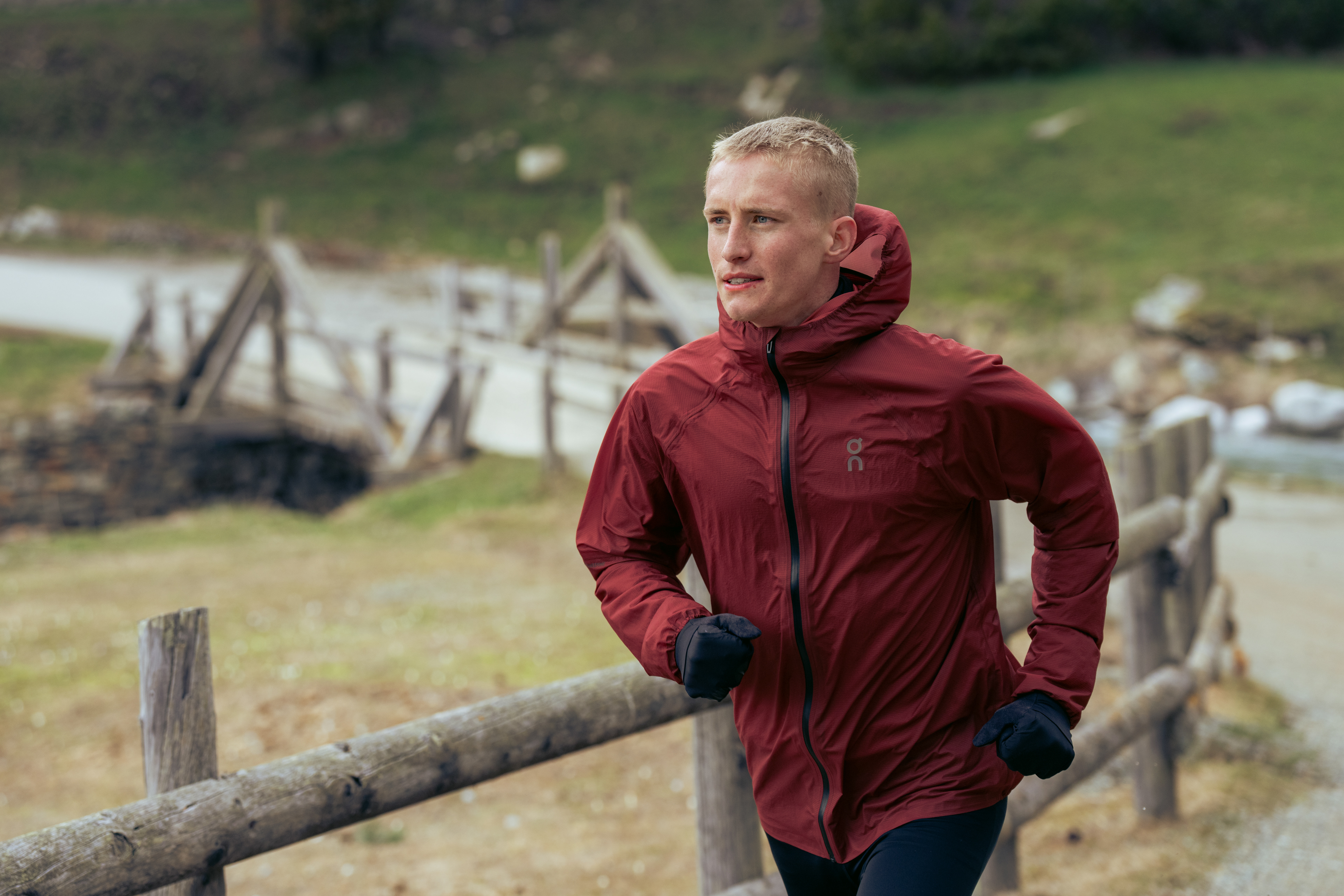 A male athlete runs along a wooden fenced dirt trail in the Alps