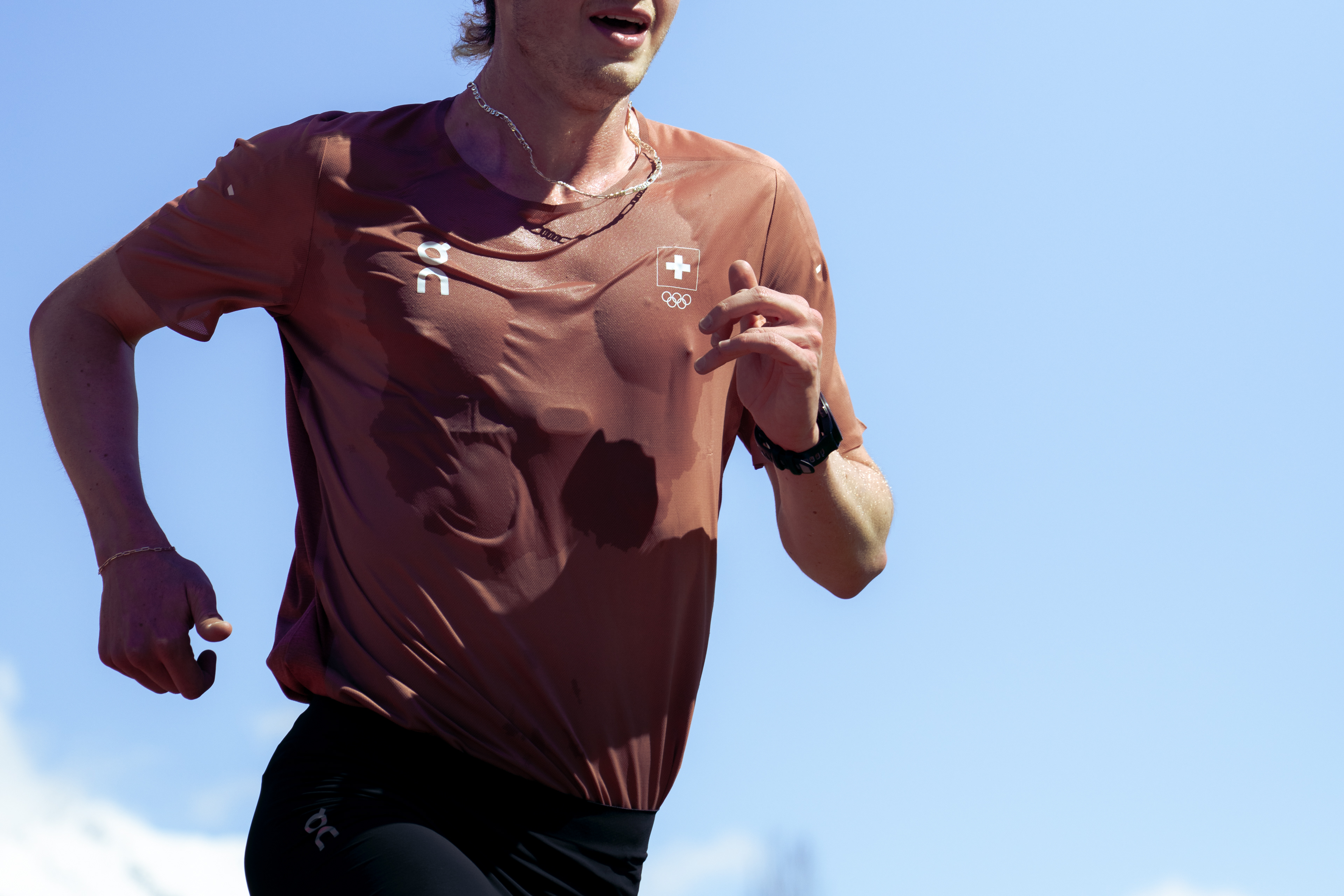 A sweaty runner moves infant of a blue sky. The photograph captures the runners torso and arms, excluding their head and legs.