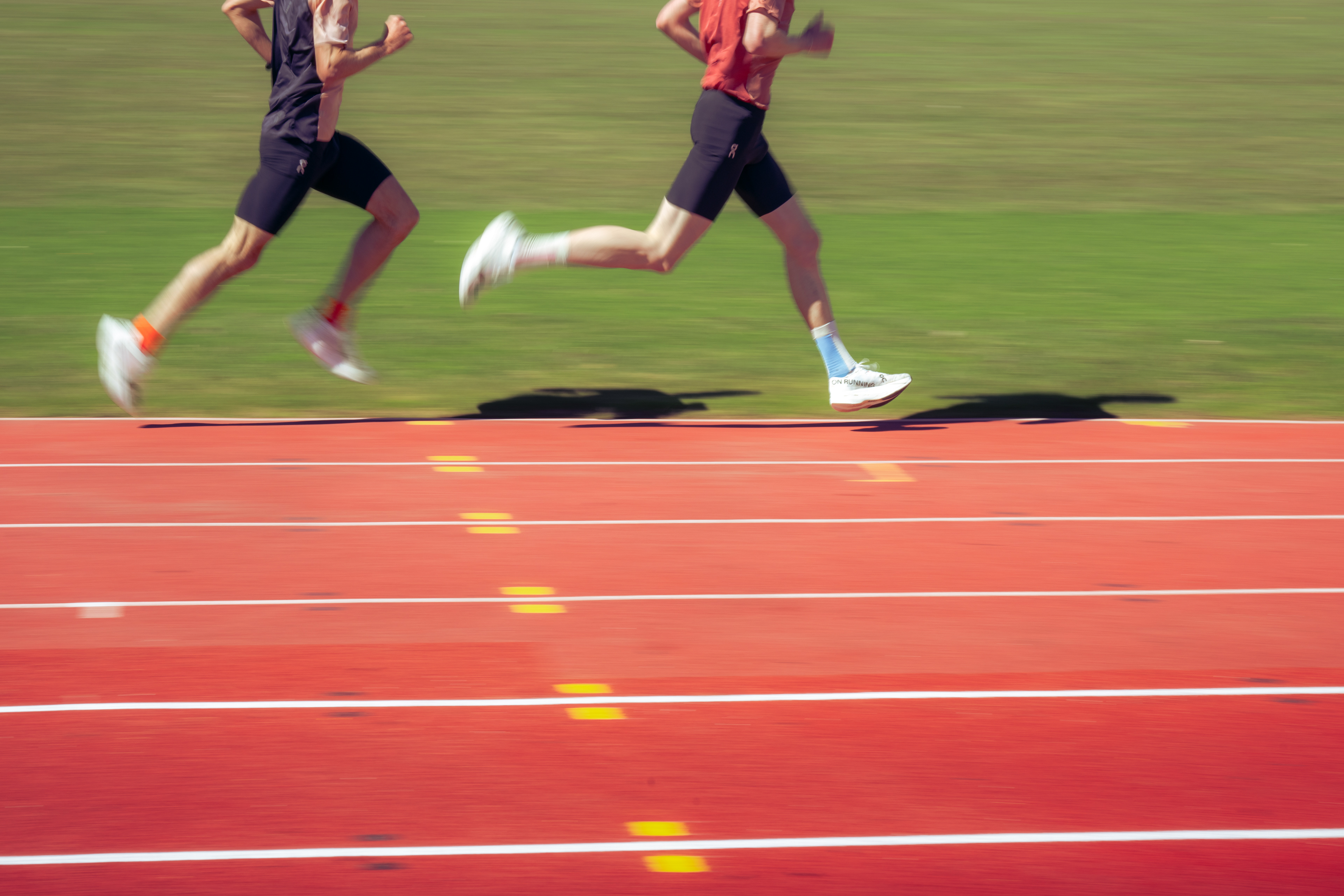 Two runners on a red running track. There is motion in the photograph, the focus is on the athletes stride.