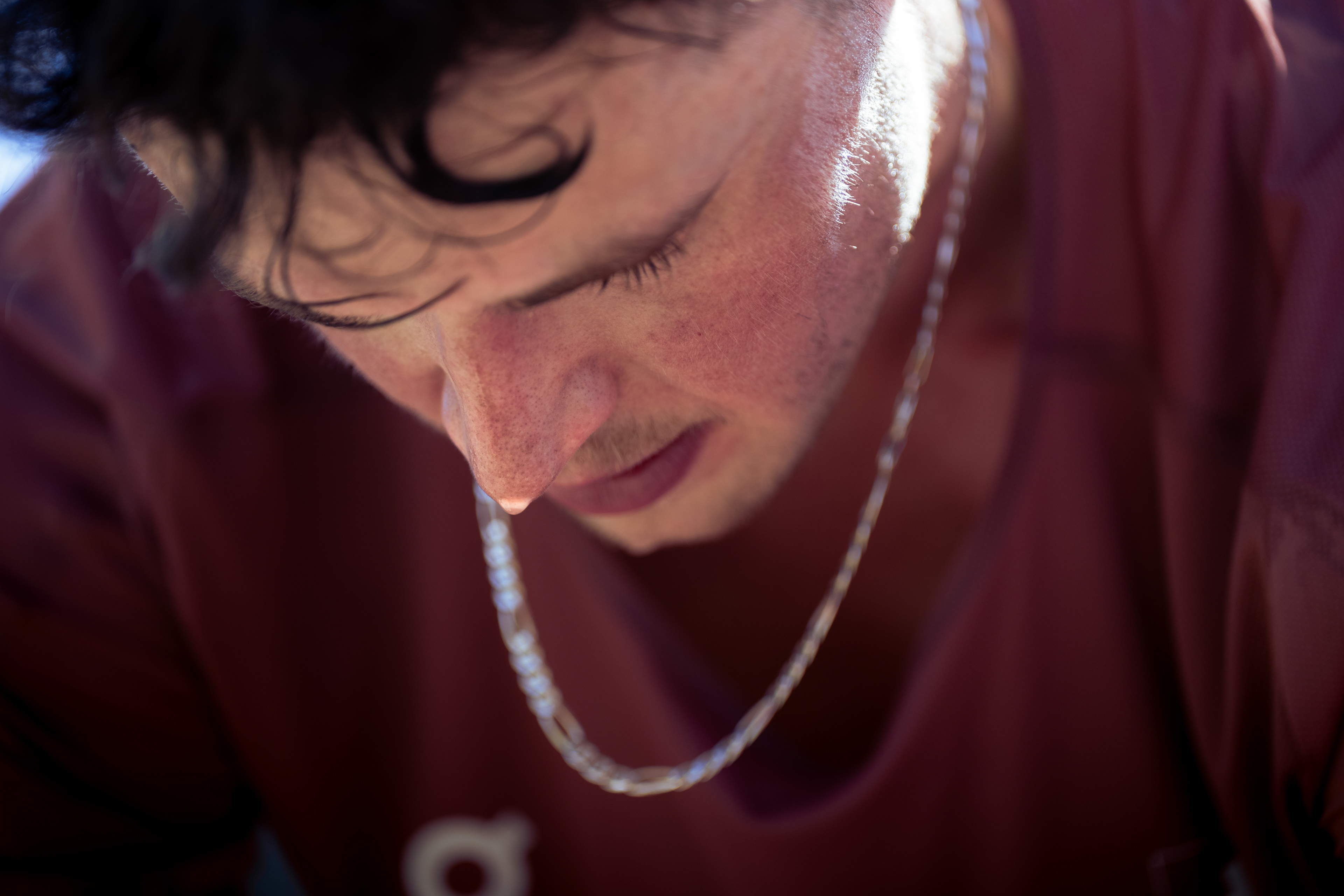 Sweat drips from a runners nose after a physical workout. The runner is bent over, leaning forward and looking toward the ground. The photo is tight on the athletes face.