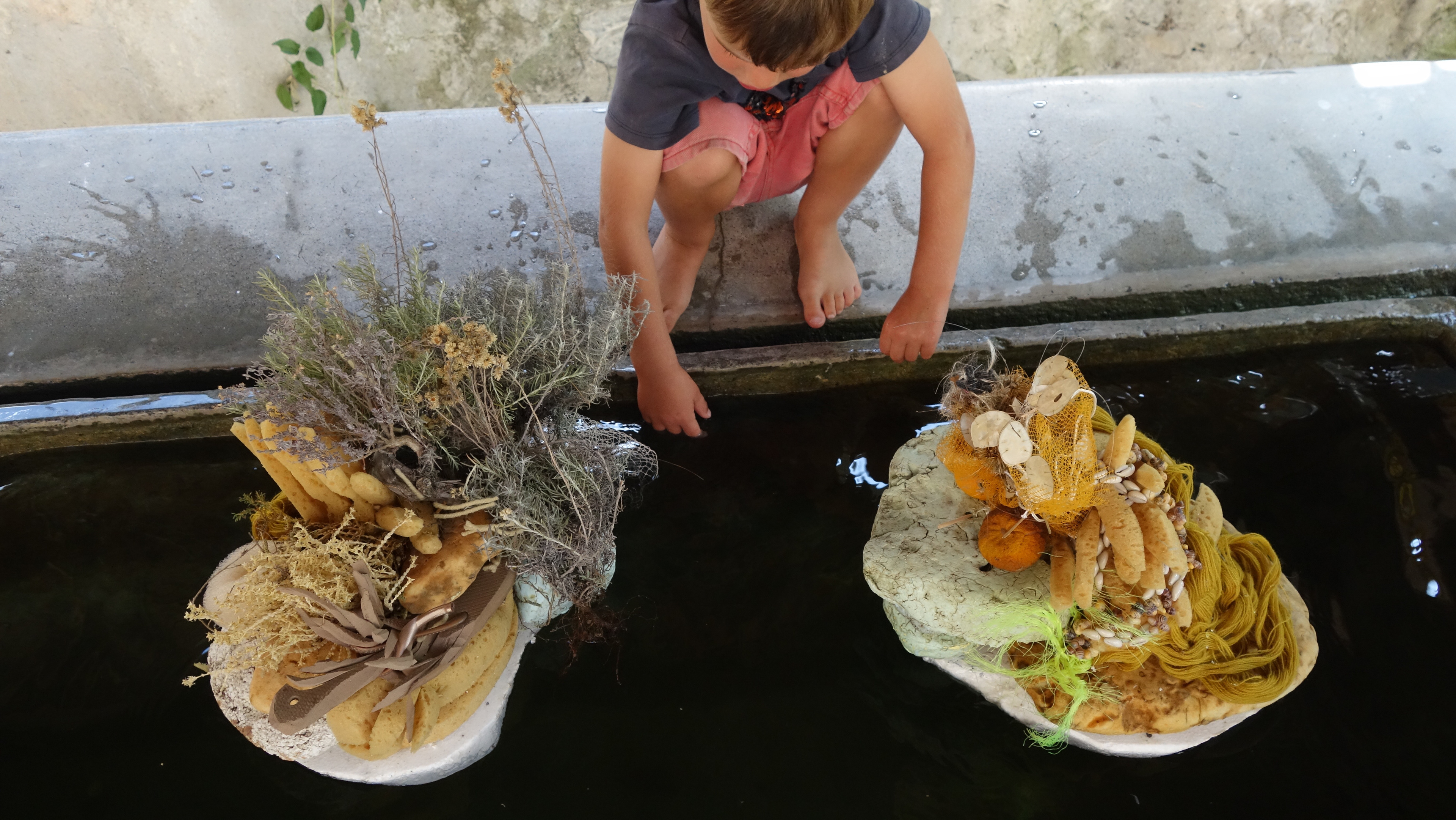 Enfant jouant dans le Diorama autour du Lavoir de Breil Sur Roya, septembre 2023Diorama autour du Lavoir,installation florale, banc pubblic recouvert de couvertures de survie