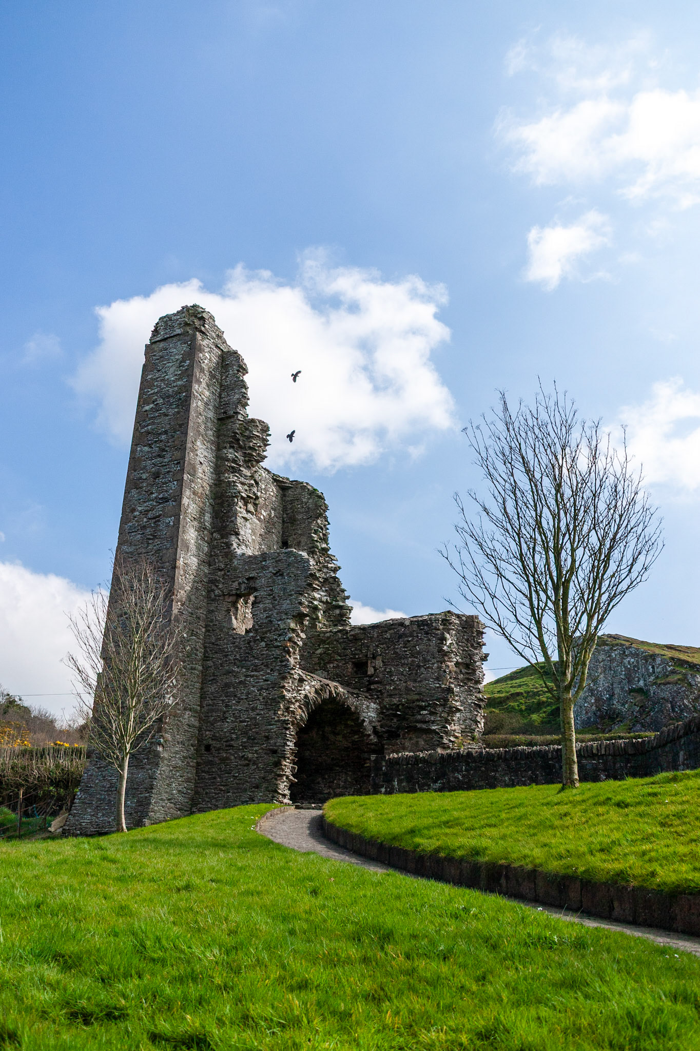 The towering stone remains of the medieval gatehouse at Mellifont Abbey in County Louth, Ireland, set against a vibrant green lawn and bright blue sky.