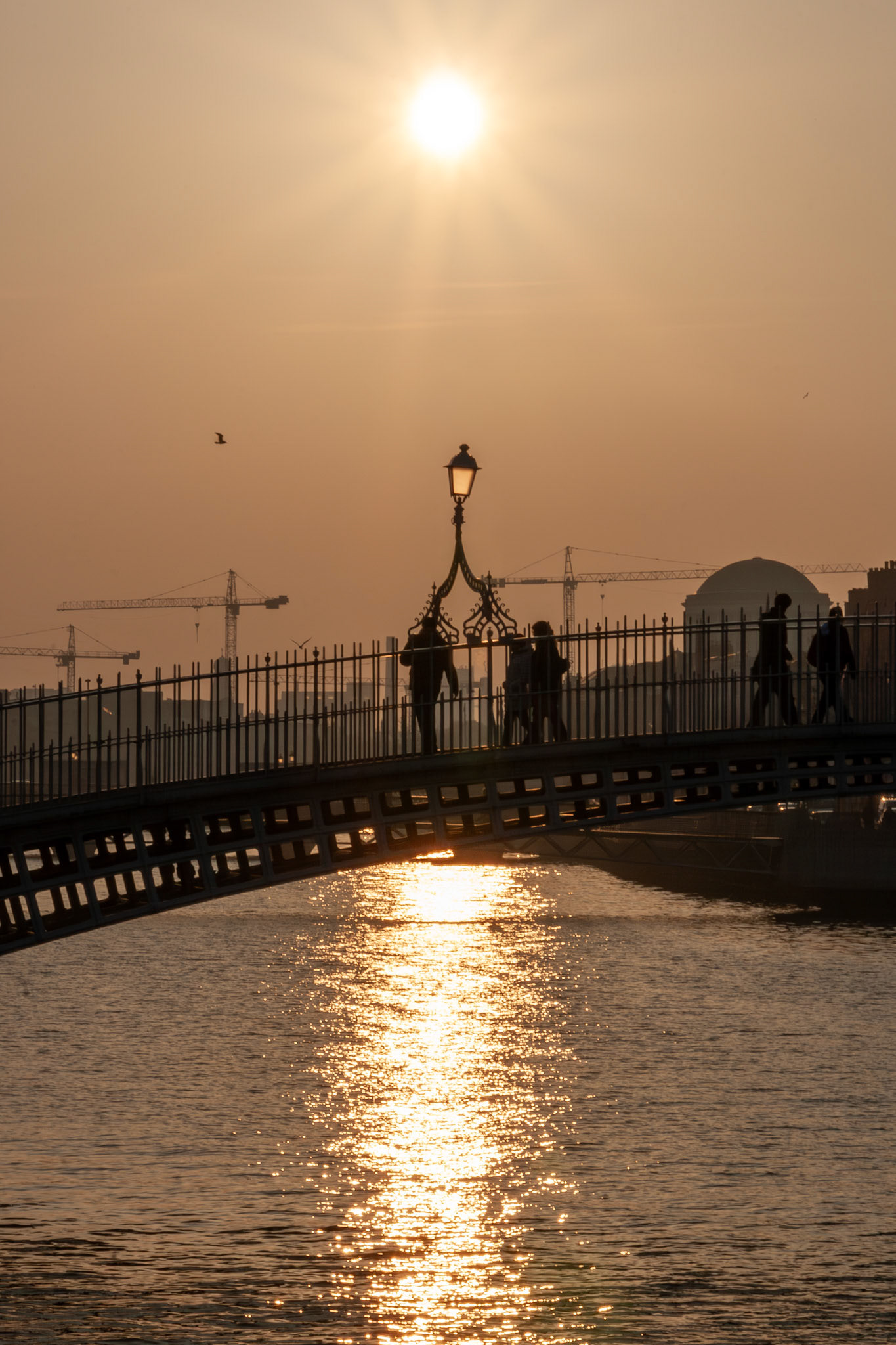 People crossing a bridge at sunset