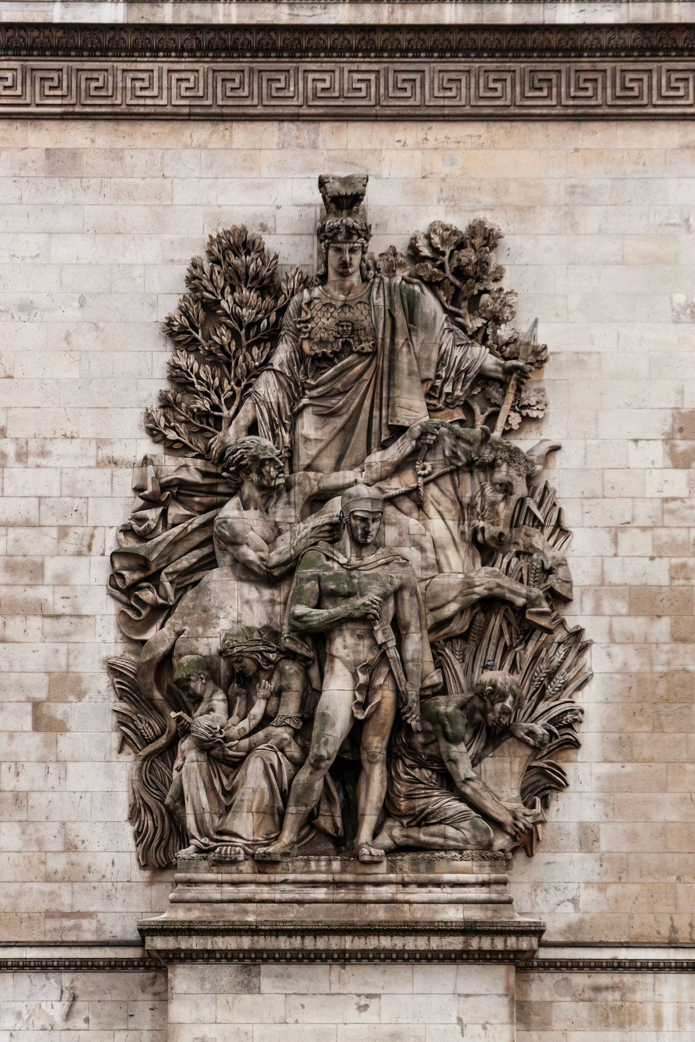 A high-detail architectural shot of "La Paix de 1815" (The Peace of 1815) by Antoine Étex, one of the four main relief sculptures on the facade of the Arc de Triomphe in Paris. The limestone carving depicts allegorical figures against a backdrop of a classic Greek fret pattern.