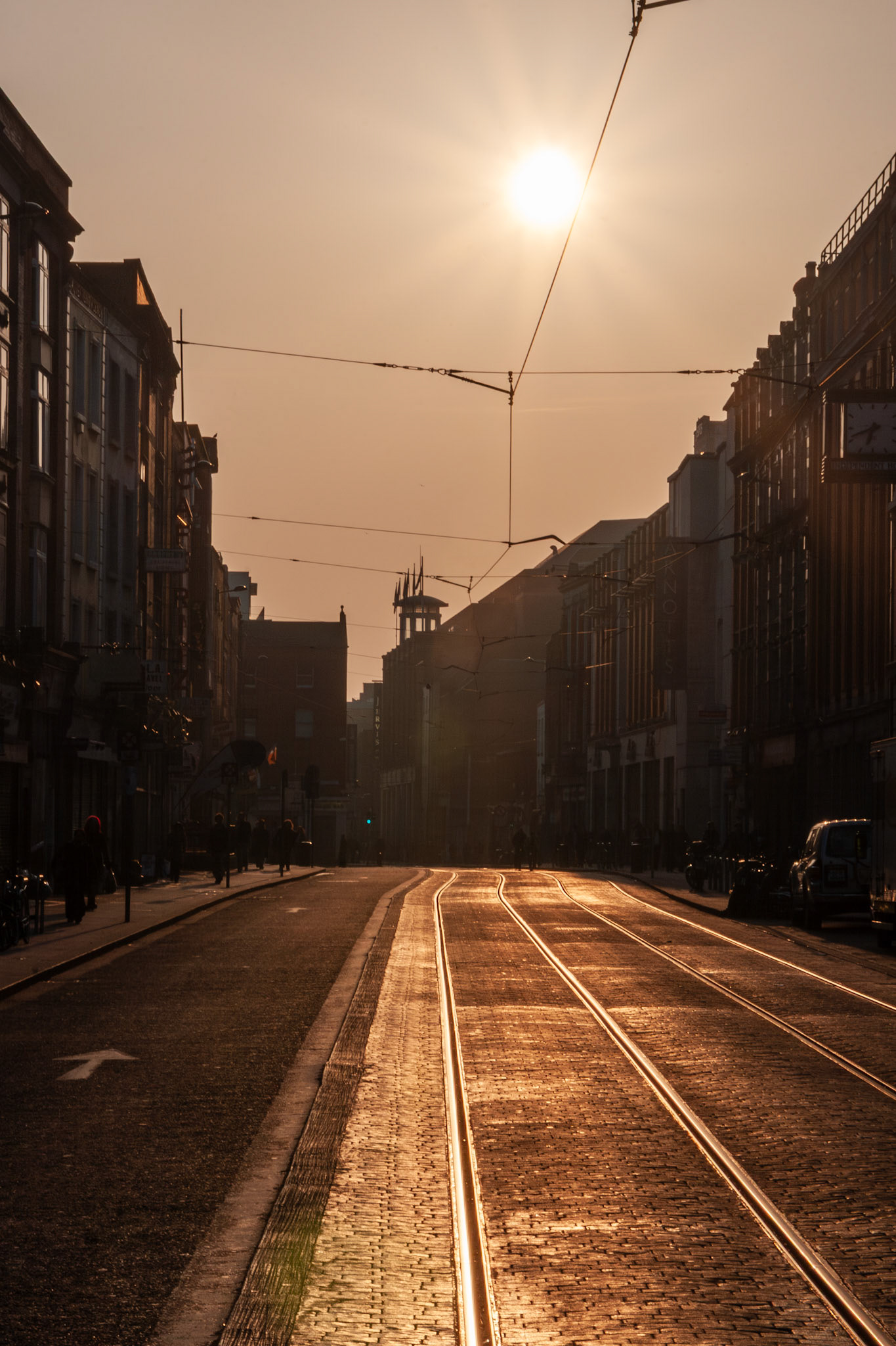 Golden hour glow over tram tracks on Middle Abbey Street in Dublin, Ireland, featuring historic architecture and soft hazy sunlight at dusk.