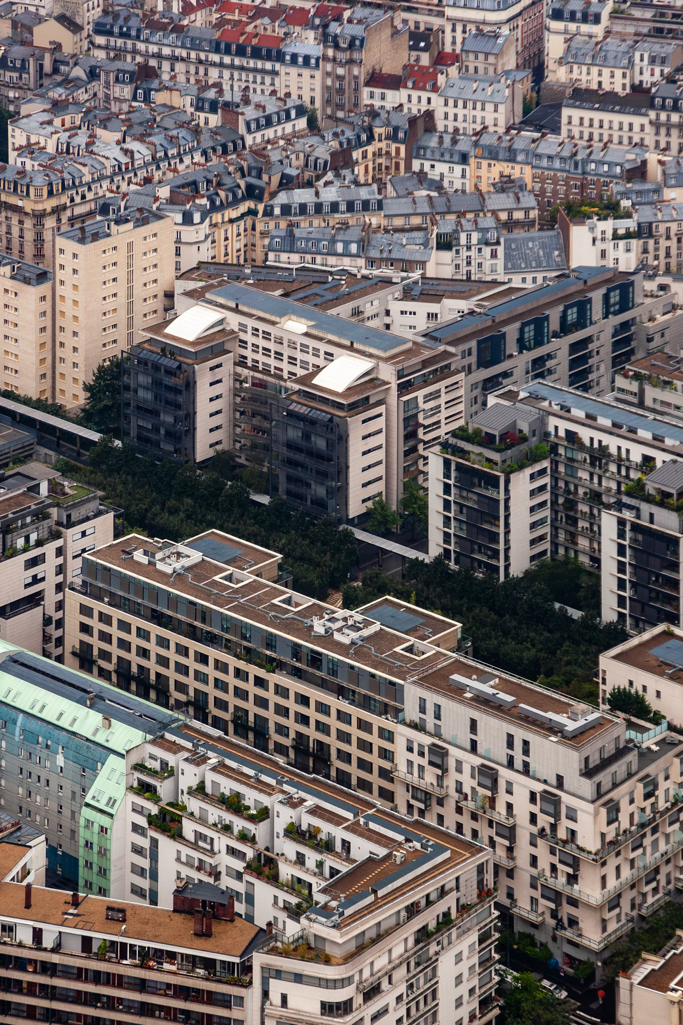 A high-angle vertical perspective showcasing the architectural diversity of Paris, France, from traditional zinc-roofed Haussmann buildings to contemporary multi-story apartment complexes with rooftop terraces.