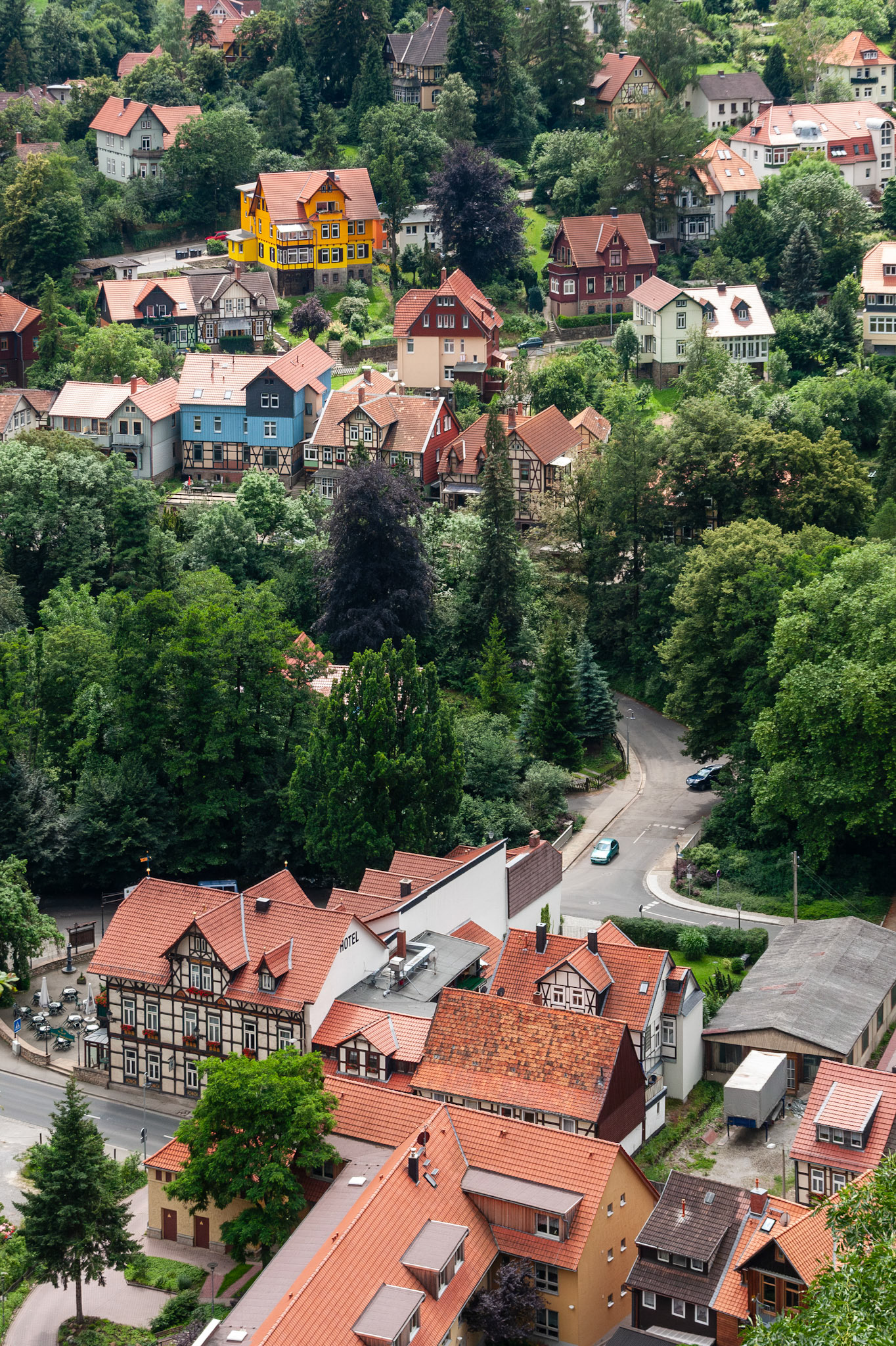 An elevated perspective of Wernigerode, Germany, showcasing a mix of traditional half-timbered architecture and modern colorful houses nestled among dense green trees in the Harz region.
