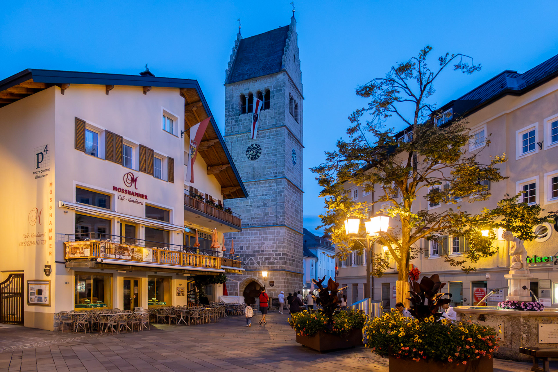 Evening street lamps illuminate the Town Square with St. Hippolyt Church and Cafe Mosshammer in Zell am See, Salzburg, Austria