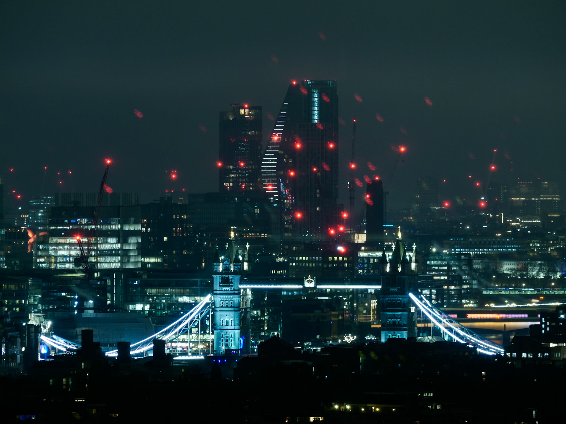 A striking night view of an illuminated Tower Bridge set against a futuristic London backdrop, featuring the Scalpel building, construction cranes, and glowing red aviation lights in a moody, cyberpunk aesthetic.