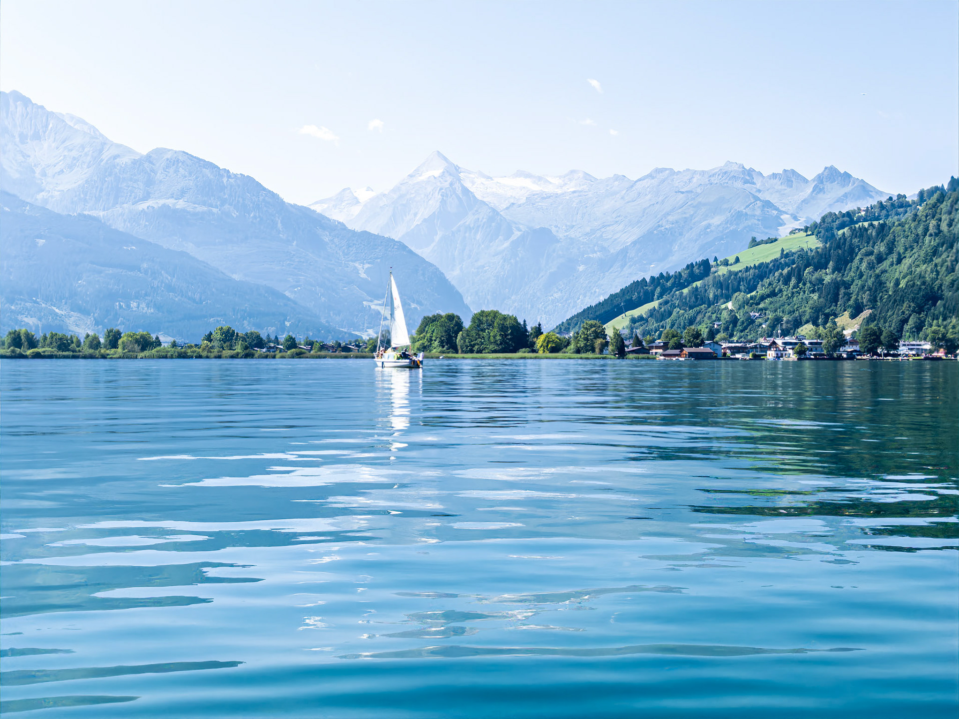Serene wave ripples reflect a sailboat and snowy Alpine peaks on lake Zell in Salzburg, Austria