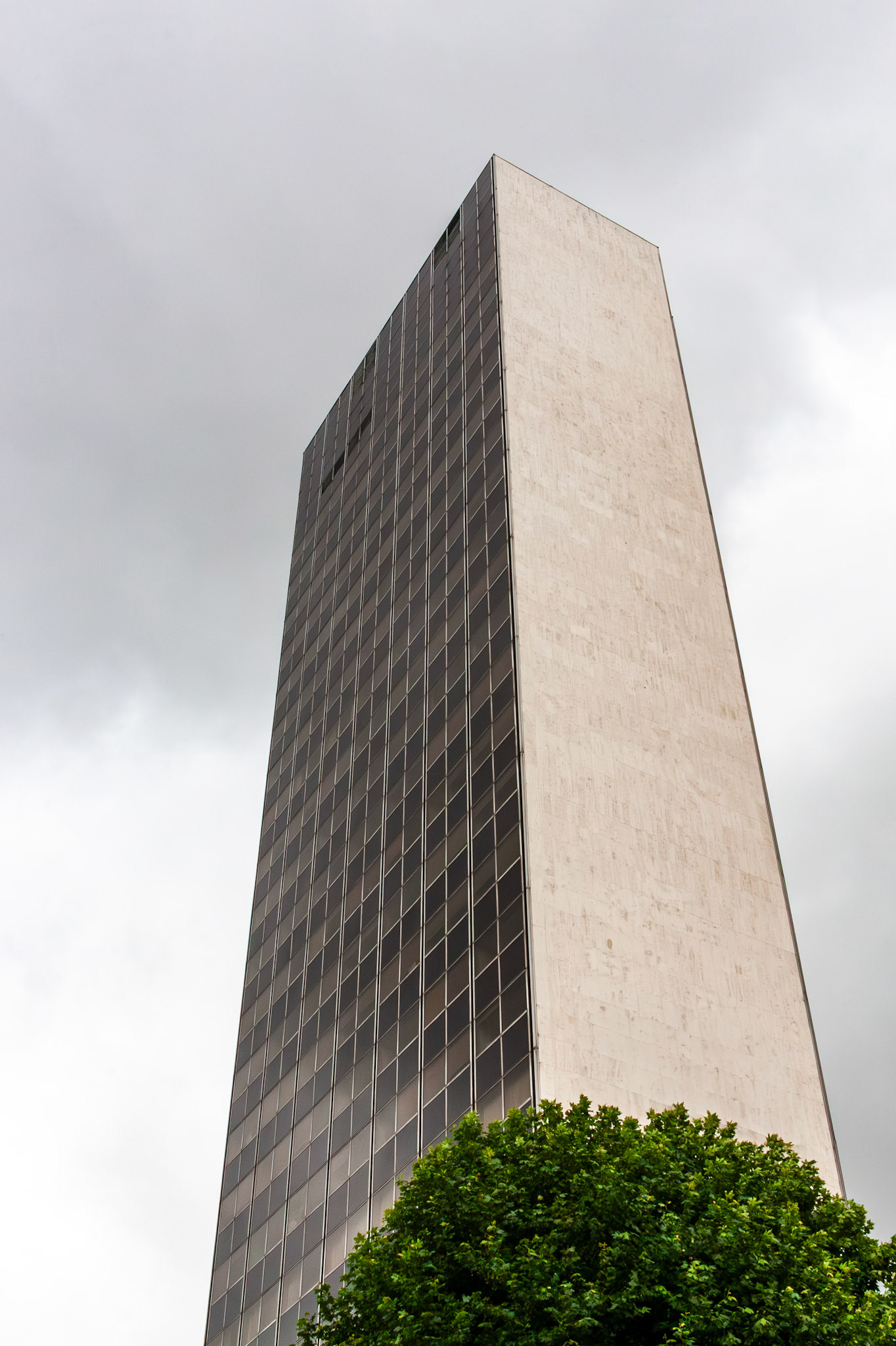 A low-angle perspective of the Tour Thiers, a prominent modernist skyscraper in Nancy, France, featuring a curtain wall of dark glass and white stone panels reaching into a gray sky.