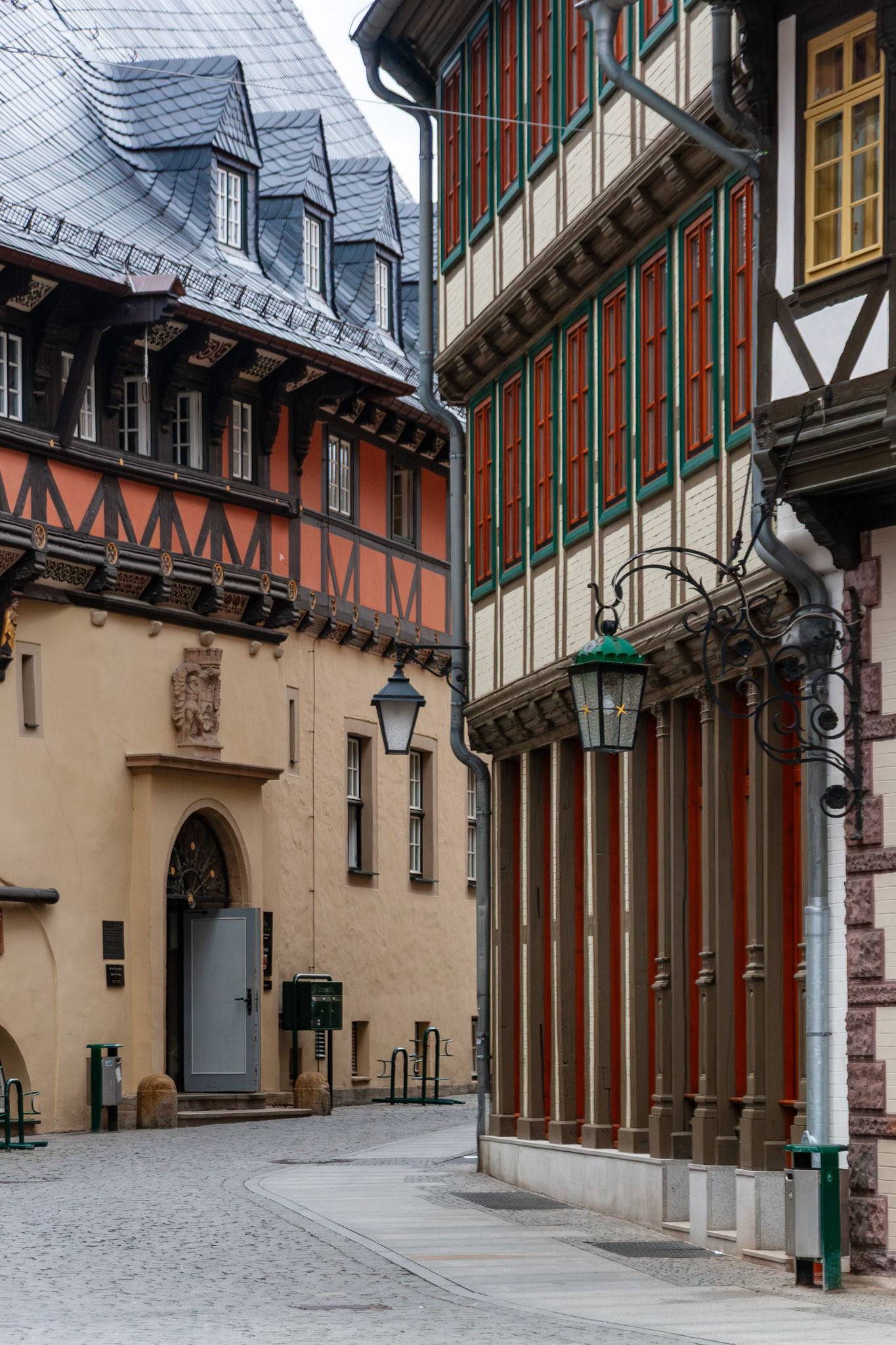 A view of a narrow cobblestone street in Wernigerode, Germany, featuring beautifully preserved half-timbered buildings with intricate wood carvings, slate-tiled roofs, and ornamental street lamps in the historic Old Town.