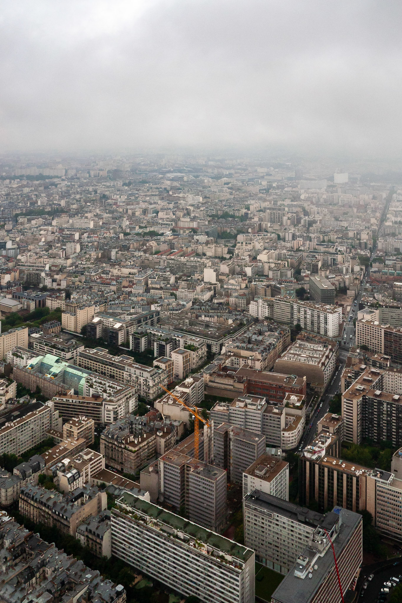 An expansive aerial view overlooking the diverse architectural landscape of Paris, France, featuring a mix of classic Haussmann buildings and modern apartment blocks under a misty, overcast sky.