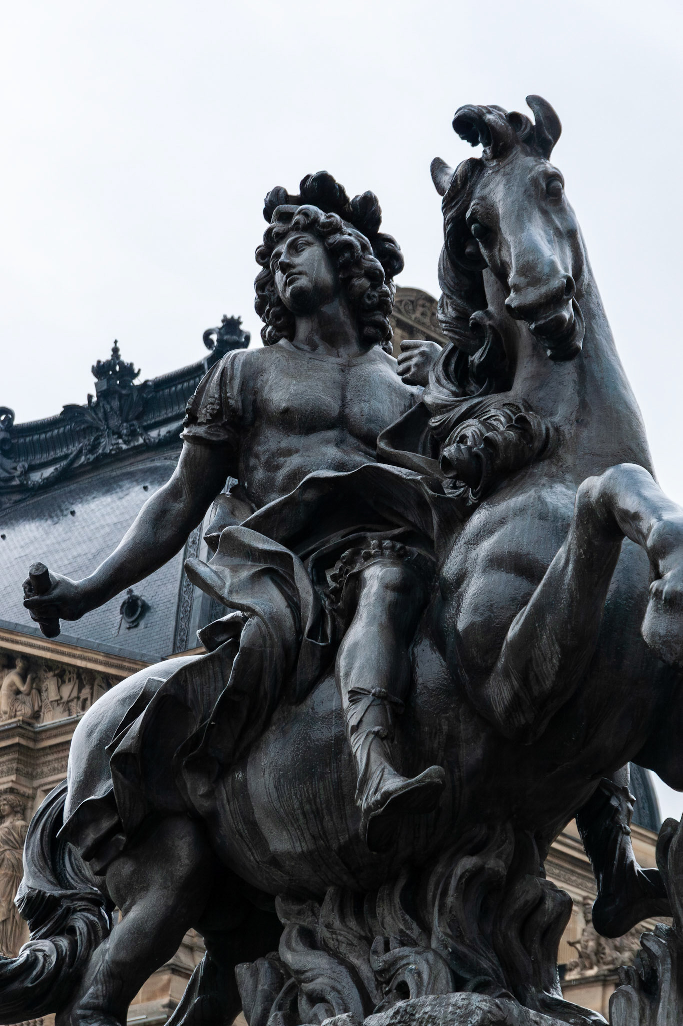 A low-angle detailed shot of a dark bronze equestrian sculpture depicting a historical figure on a horse, set against the backdrop of ornate French architecture and a bright sky.