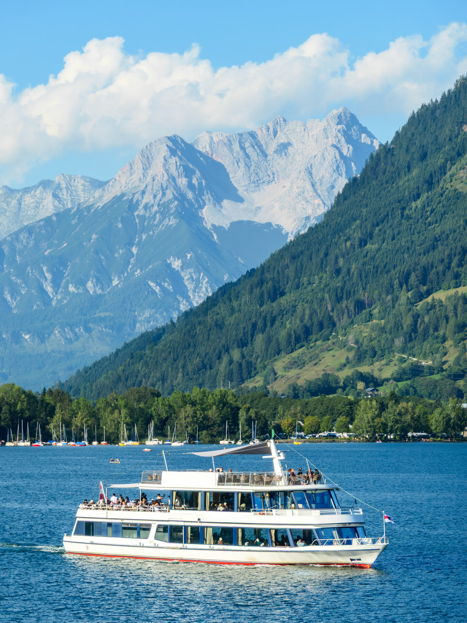 White and red passenger ship on lake Zell surrounded by Alpine peaks on a sunny day at Zell Am See, Salzburg, Austria