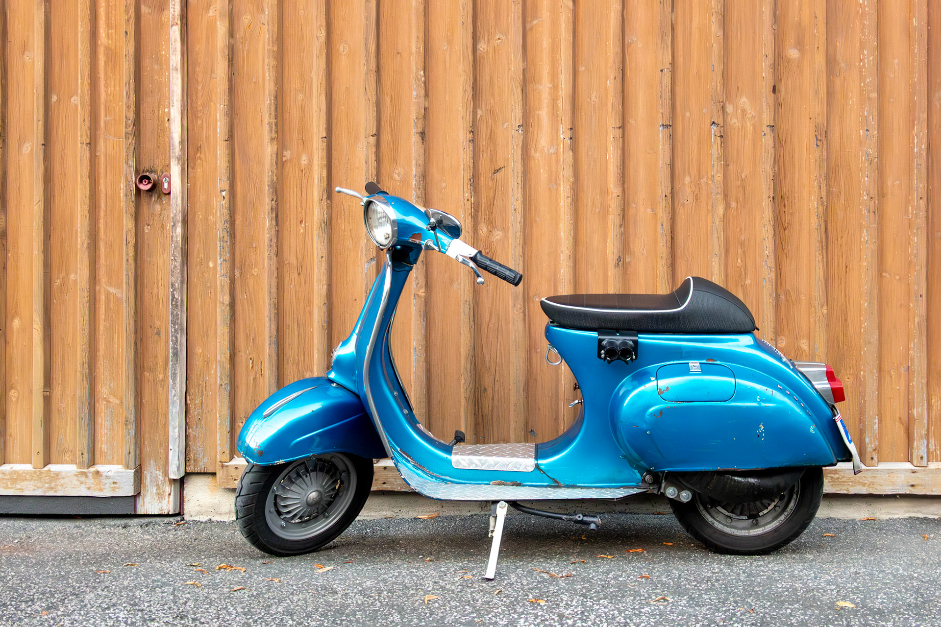 Retro classic blue scooter parked against an orange wooden wall