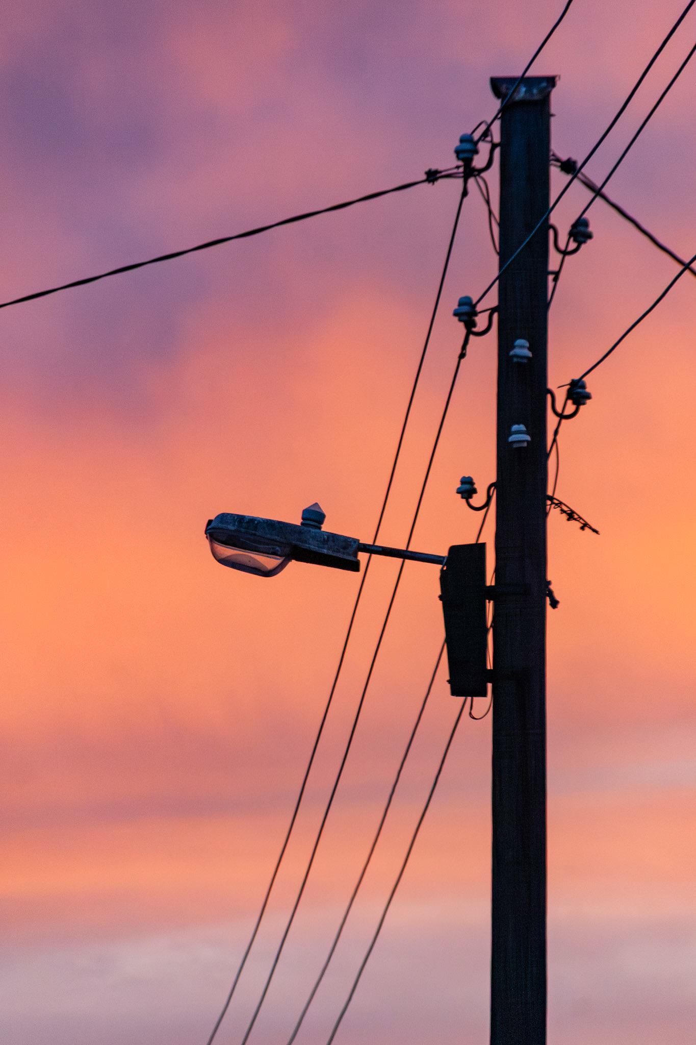 A dramatic vertical composition featuring the silhouette of a utility pole and street lamp set against a vivid, multi-colored sky during a deep sunset in Dublin, Ireland.