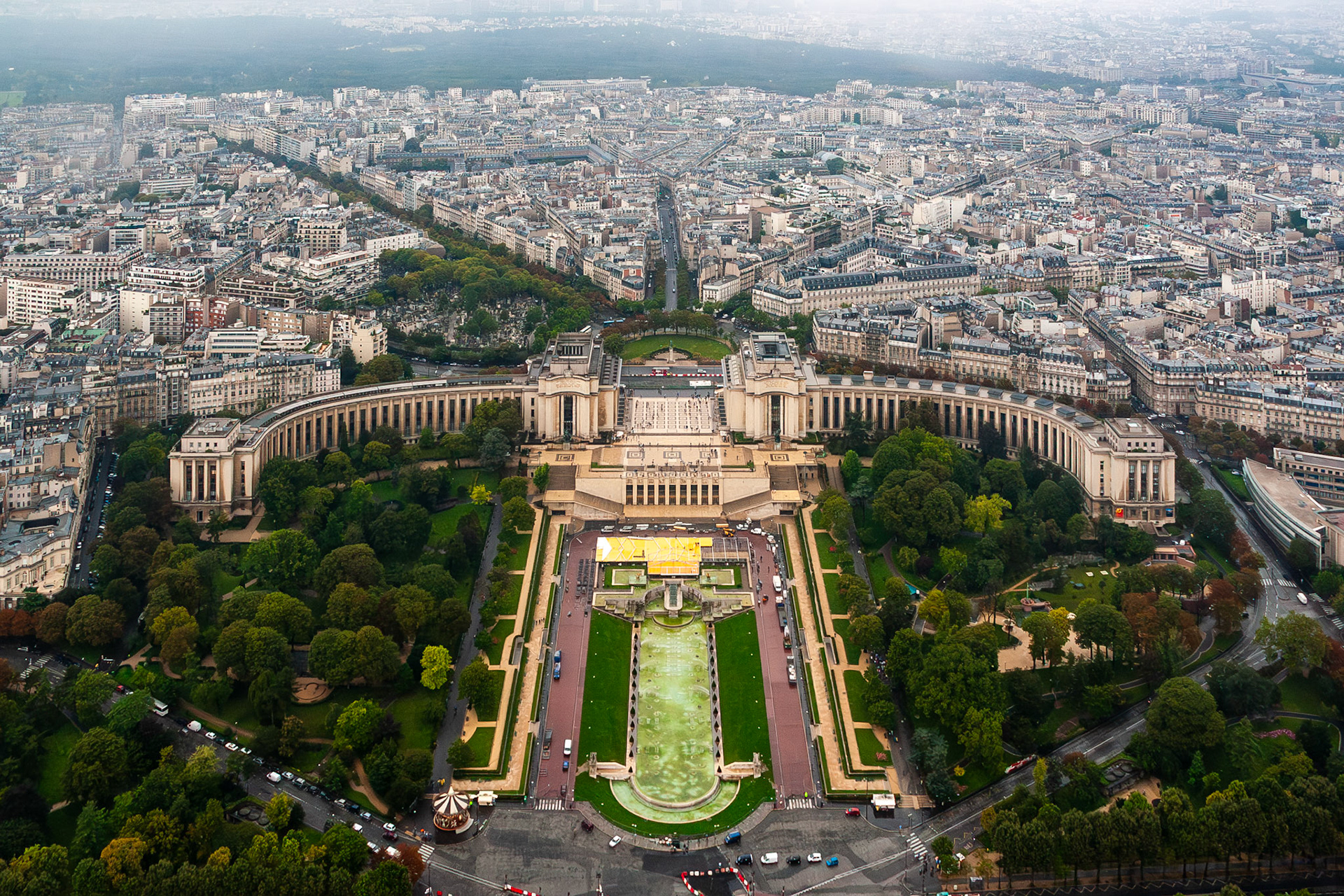 A breathtaking high-angle panorama of the Trocadéro Gardens and the curved Palais de Chaillot, looking toward the urban sprawl and symmetrical street layout of Paris, France.