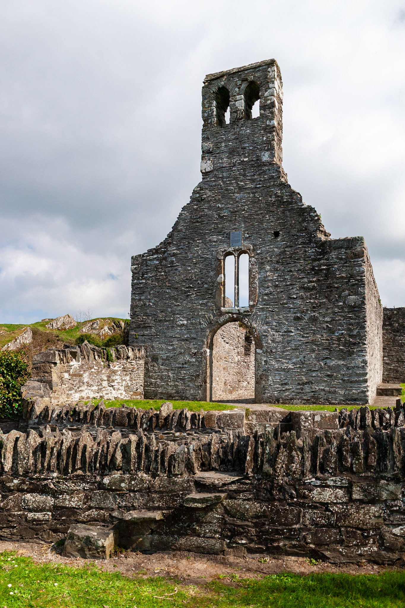 The weathered stone remains of Mellifont Abbey, Ireland's first Cistercian monastery, showcasing the historic bell tower and arched windows against a cloudy sky.