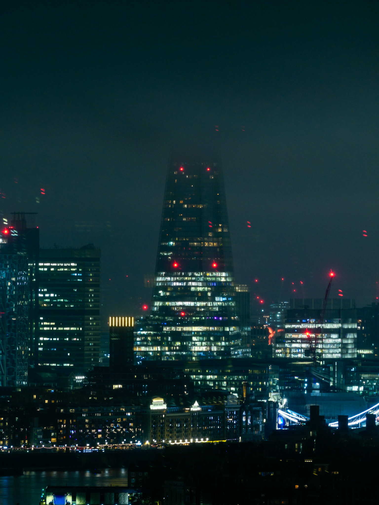 A moody, cyberpunk-inspired night view of The Shard in London, with the iconic glass skyscraper partially shrouded in mist and illuminated by city lights and glowing red aviation beacons.