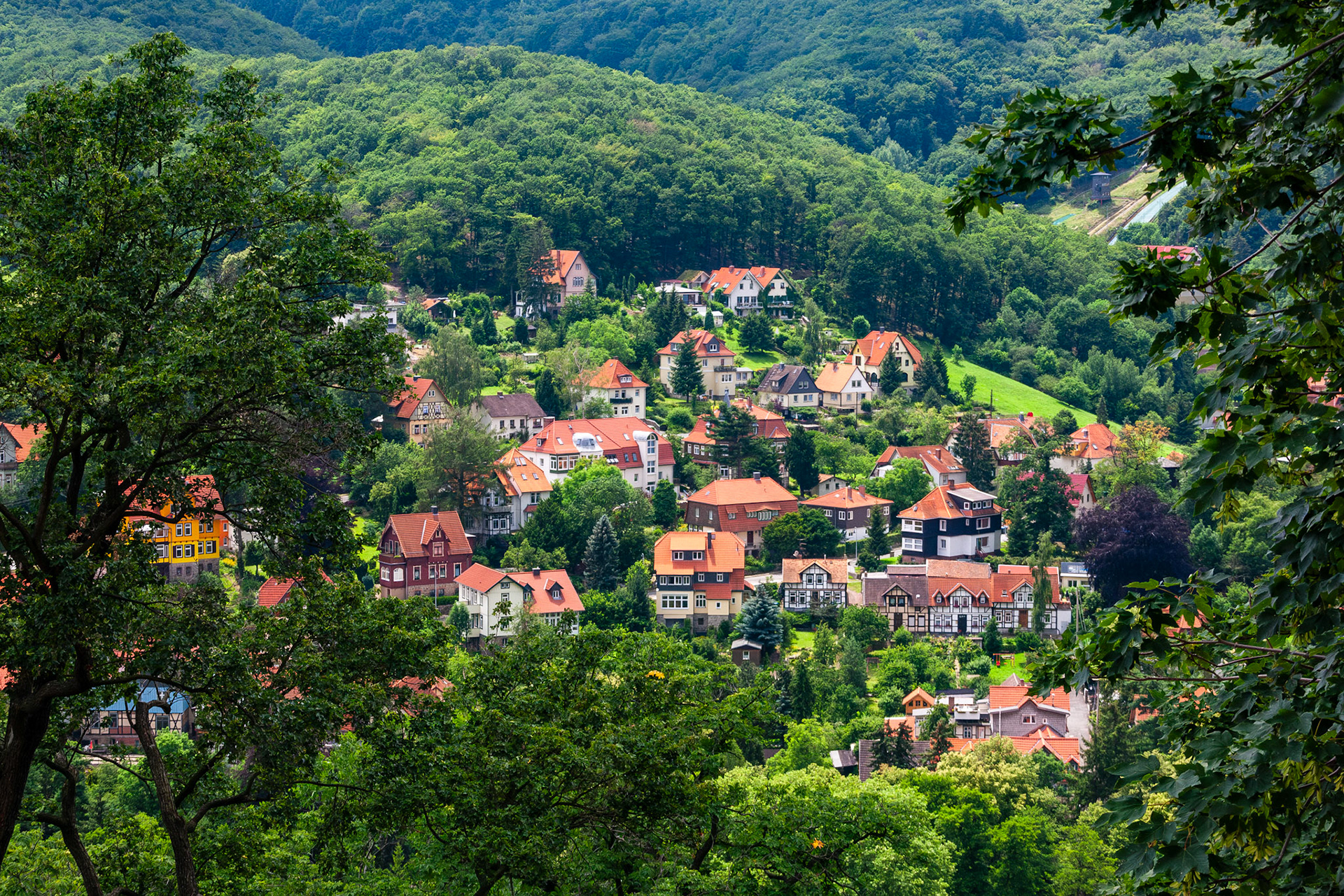 A scenic high-angle view of traditional German houses with red-tiled roofs nestled among lush green forests and rolling hills in the picturesque town of Wernigerode, Germany.