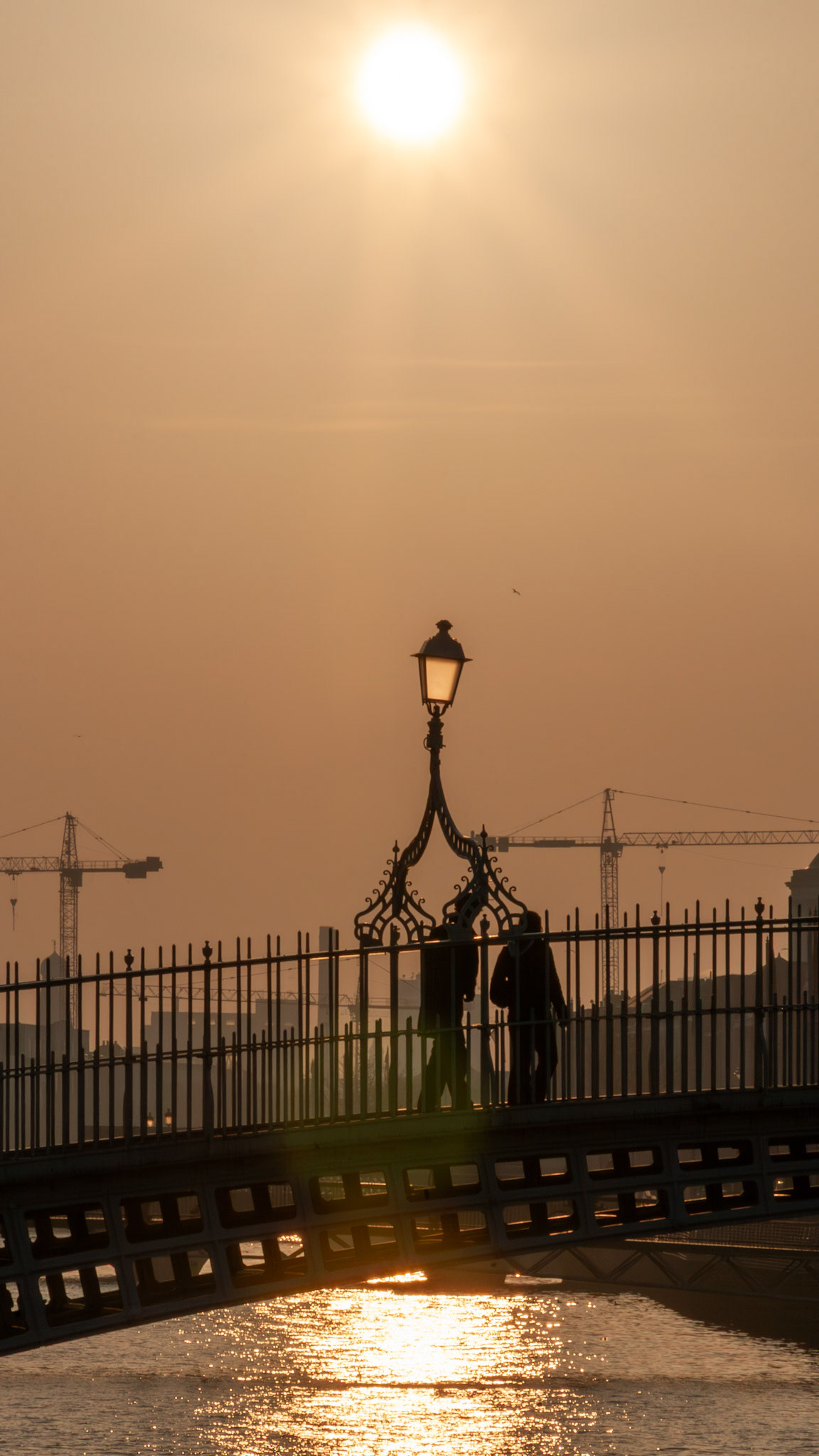 People crossing a bridge at sunset