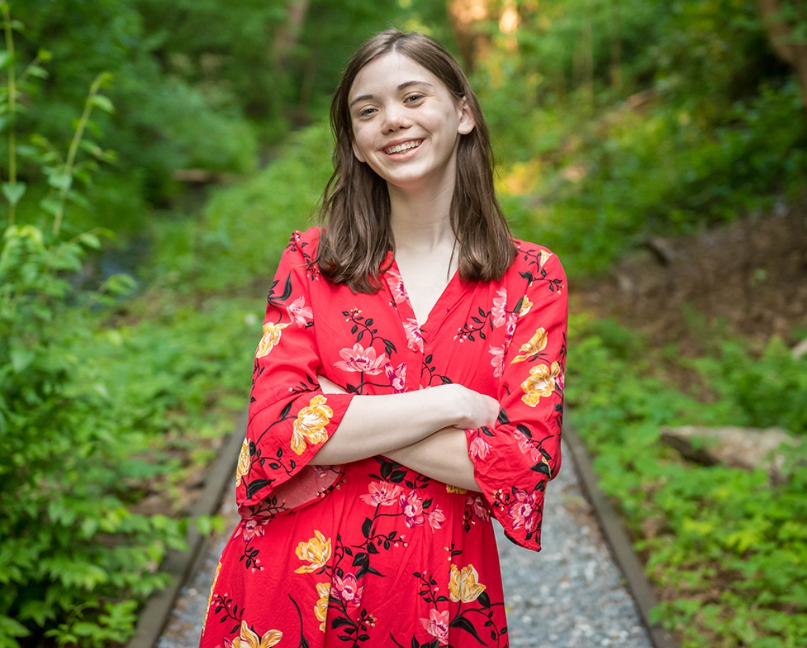 Patricia "Patch" Hatley arms crossed in a pose, train tracks and nature behind her.