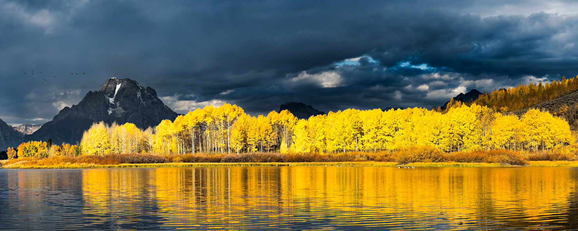 As I drove up to Oxbow Bend for my second weekend-long attempt to photograph the famous location, I was disappointed to see that the sky was again completely overcast – foiling any chance for the sunrise that I hoped to capture. Since this would be my last opportunity to capture this scene before the leaves fell, I packed up my gear and headed out simply hoping for a miracle. I arrived at the bend and made my way to my previously chosen spot. I knew it well by now. There were a few other hopefuls like myself that morning, but far fewer than usual.The hours passed silently, and the scene was as beautiful as always. The geese called, elk bugled in the distance, and we exchanged stories about other shots we had acquired during the season while waiting for a sunrise that came and passed without announcement.Slowly, photographers began to pack their gear and head for the other locations they had scouted previously. I thought about turning in as well, but for the past two weeks I had only one goal in mind. I decided to wait. The clouds were moving quickly and occasionally a patch of sunlight would make its way through, so I was hopeful. Suddenly, and out of nowhere – the clouds opened up and lit up the scene! It was everything I hoped for. Quickly, I fired my sequence. Going right; one, two, three, four, five, sweeping back, but the light was gone as quickly as it had arrived. At the moment, I couldn’t know for sure. I stayed a few more minutes, then packed up my gear and headed out - but in my heart I was sure I had captured something truly special.