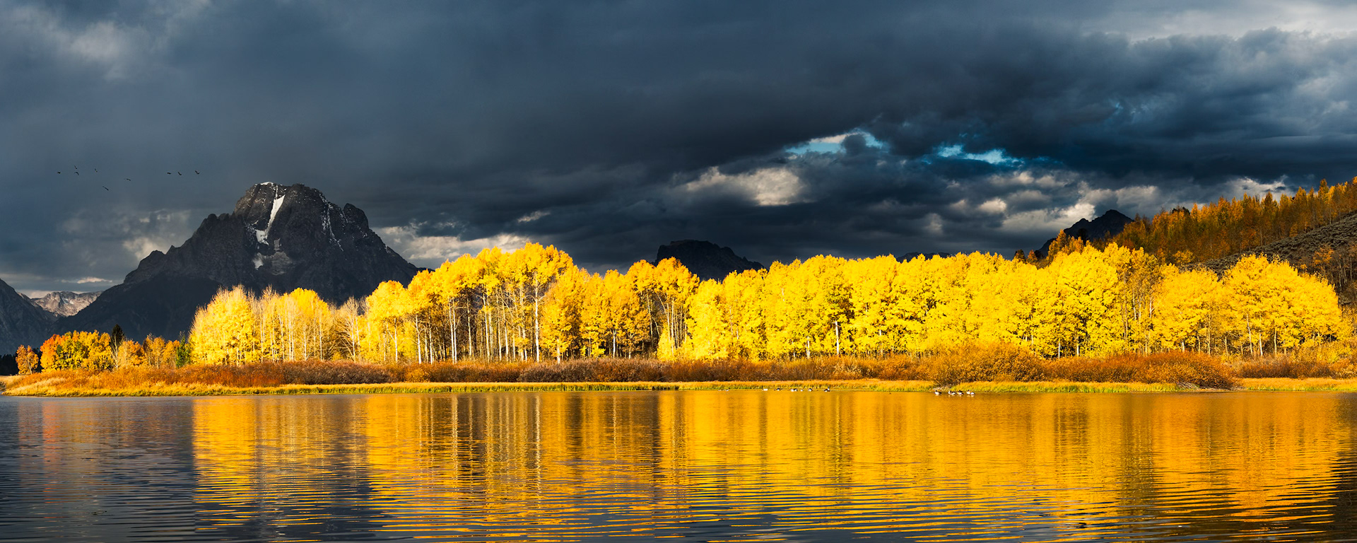 As I drove up to Oxbow Bend for my second weekend-long attempt to photograph the famous location, I was disappointed to see that the sky was again completely overcast – foiling any chance for the sunrise that I hoped to capture. Since this would be my last opportunity to capture this scene before the leaves fell, I packed up my gear and headed out simply hoping for a miracle. I arrived at the bend and made my way to my previously chosen spot. I knew it well by now. There were a few other hopefuls like myself that morning, but far fewer than usual.The hours passed silently, and the scene was as beautiful as always. The geese called, elk bugled in the distance, and we exchanged stories about other shots we had acquired during the season while waiting for a sunrise that came and passed without announcement.Slowly, photographers began to pack their gear and head for the other locations they had scouted previously. I thought about turning in as well, but for the past two weeks I had only one goal in mind. I decided to wait. The clouds were moving quickly and occasionally a patch of sunlight would make its way through, so I was hopeful. Suddenly, and out of nowhere – the clouds opened up and lit up the scene! It was everything I hoped for. Quickly, I fired my sequence. Going right; one, two, three, four, five, sweeping back, but the light was gone as quickly as it had arrived. At the moment, I couldn’t know for sure. I stayed a few more minutes, then packed up my gear and headed out - but in my heart I was sure I had captured something truly special.