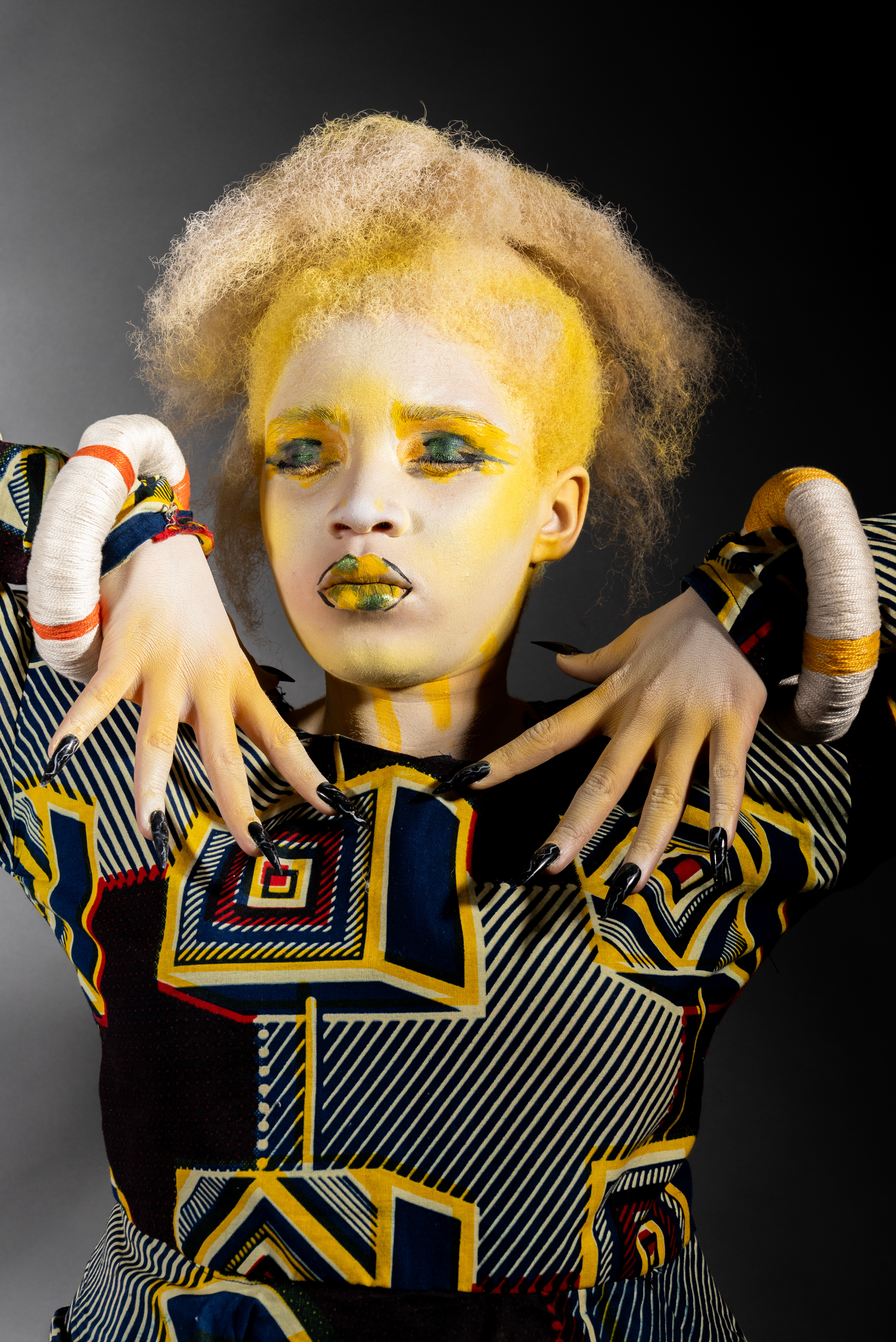 Modelo albina con ojos claros, retratada en pose de tres cuartos, con cuerpo pintado con body painting que simula ropa africana tradicional. 