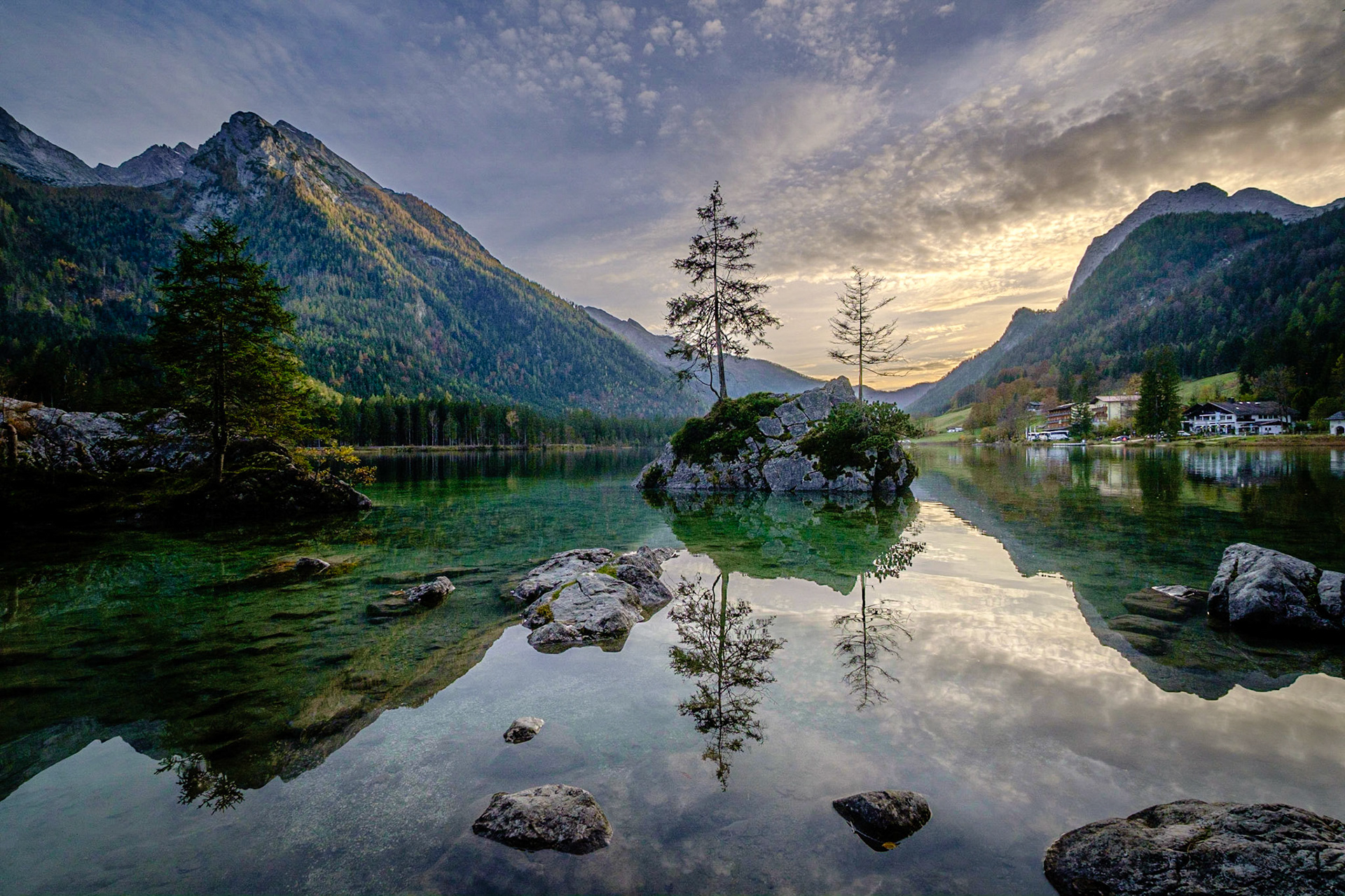 At Hintersee in Bavaria’s Berchtesgaden region, a tiny tree-clad island floats in crystal-clear waters, mirroring the rugged Watzmann peaks and dramatic evening skies.