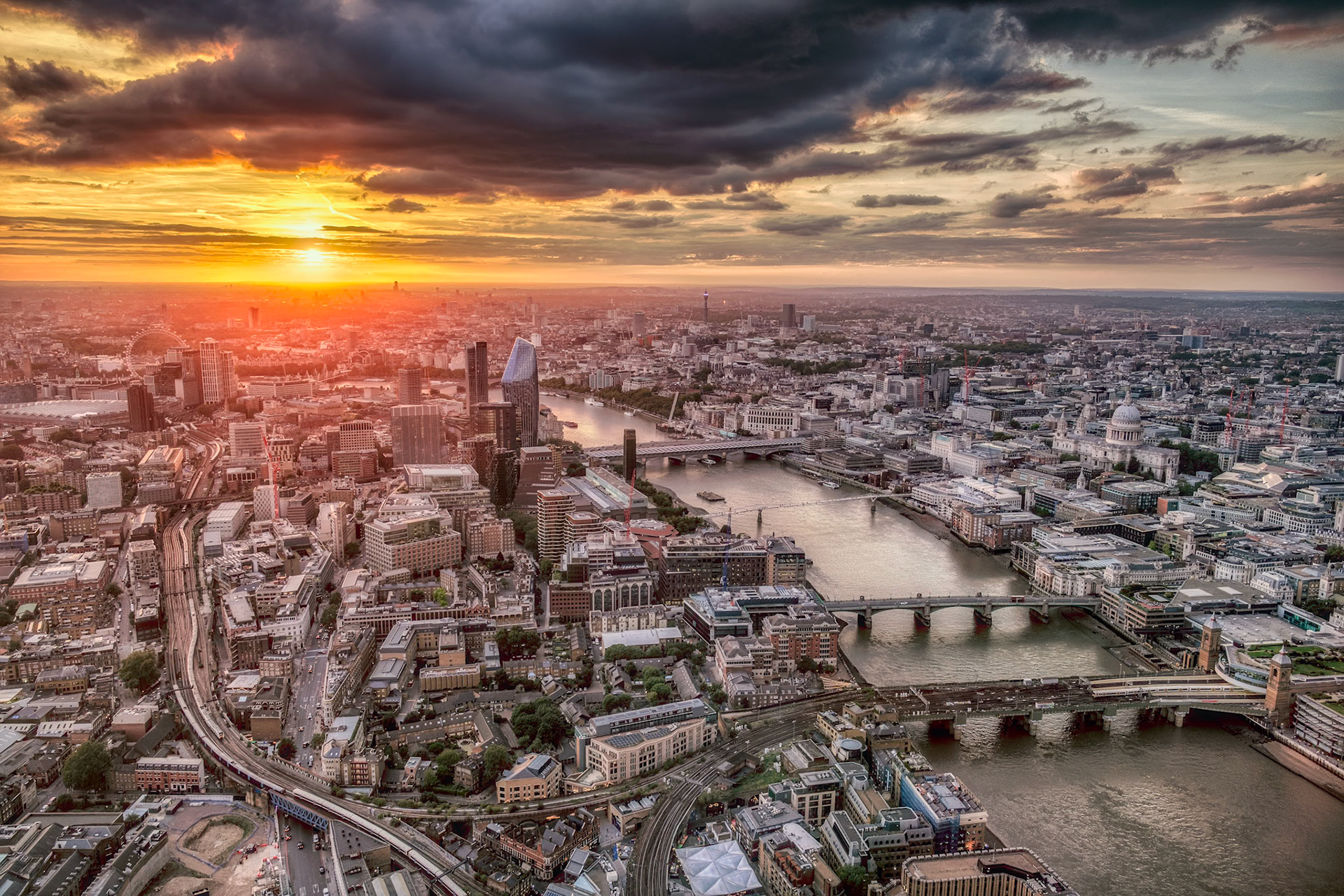 A sweeping aerial of London at sunset shows the Thames winding past Waterloo and Blackfriars bridges as the city skyline glows under golden light.