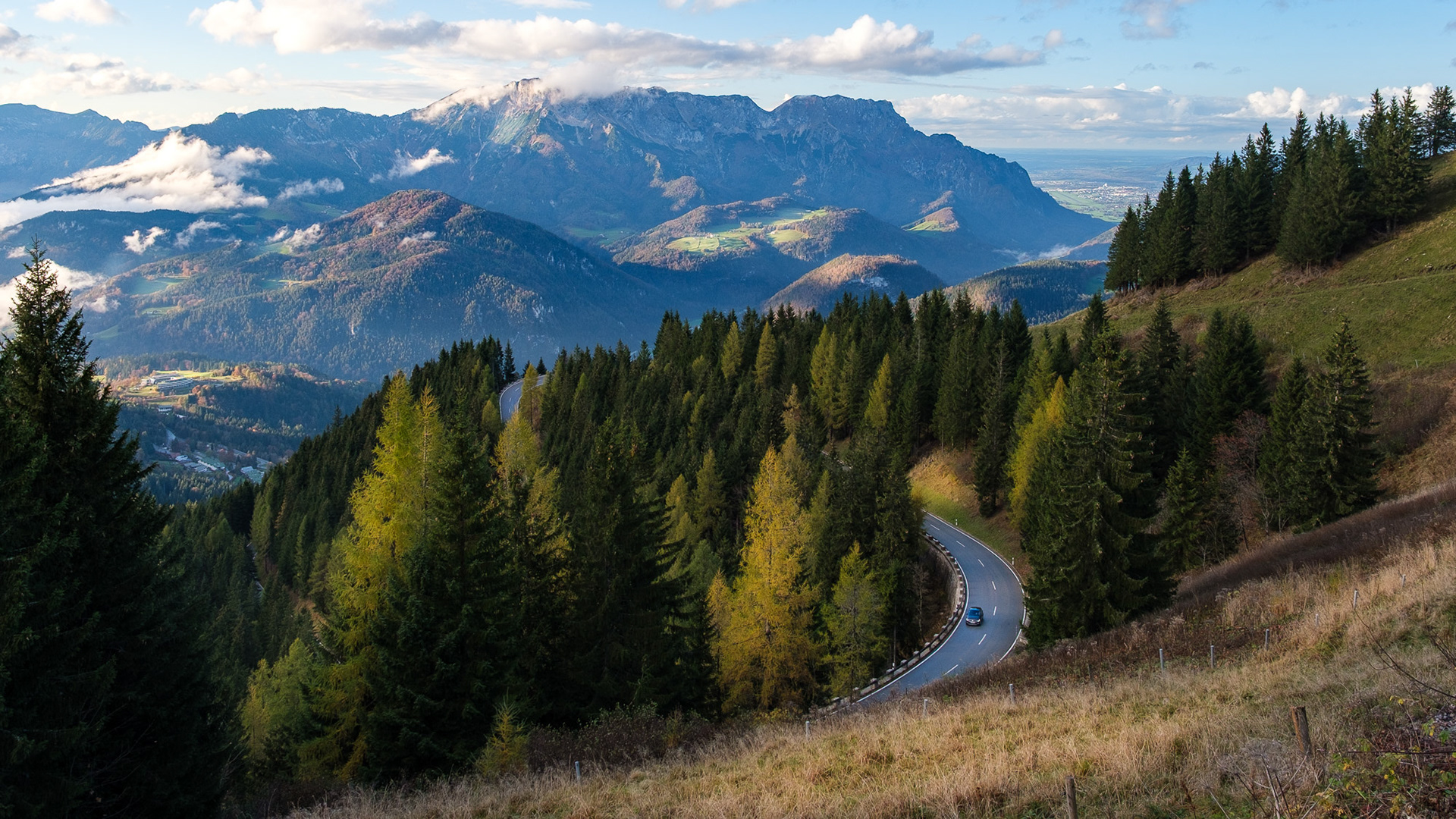 Winding mountain road through alpine forest in Berchtesgaden, Germany, with layers of mountains in soft afternoon light.