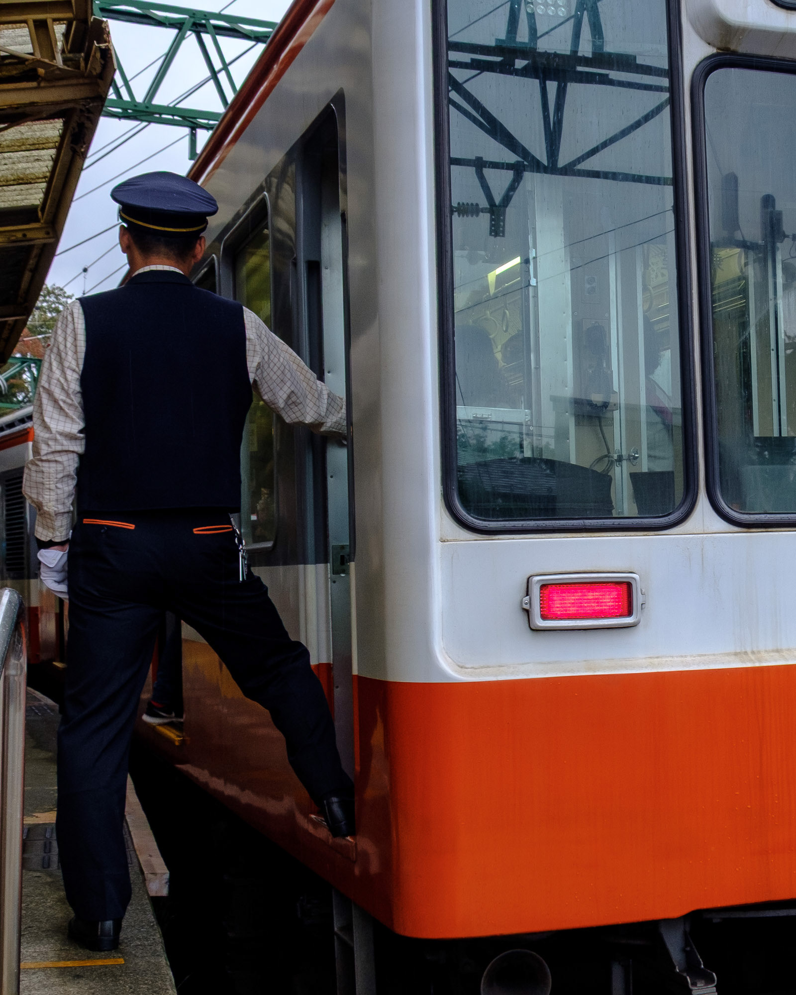 A Hakone Tozan Railway conductor stepping onto the train, holding the door frame as the carriage prepares to depart.