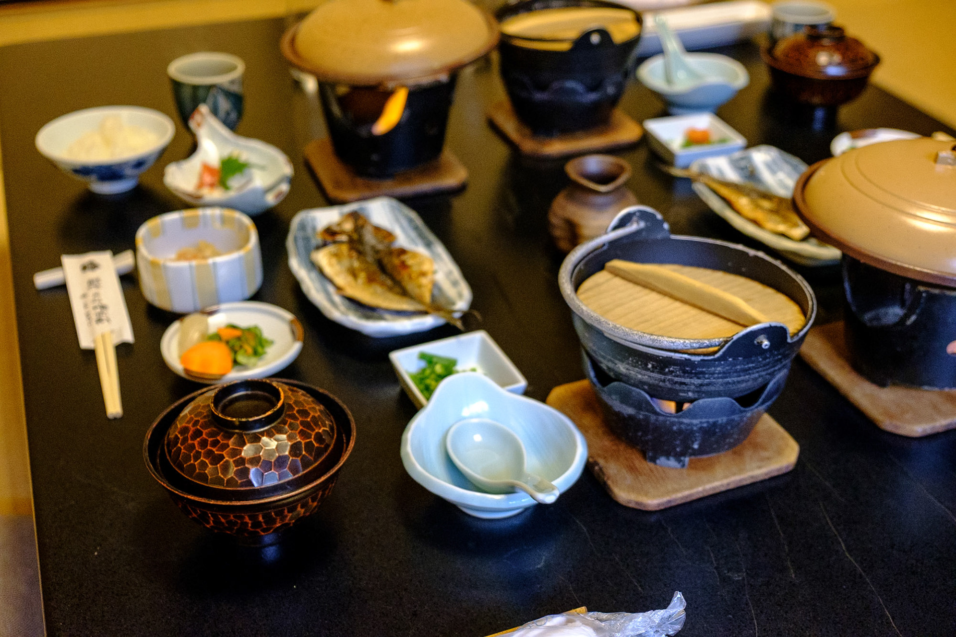 A traditional Japanese breakfast with small dishes, grilled fish, rice, miso soup and hot pots arranged on a low table in a ryokan.