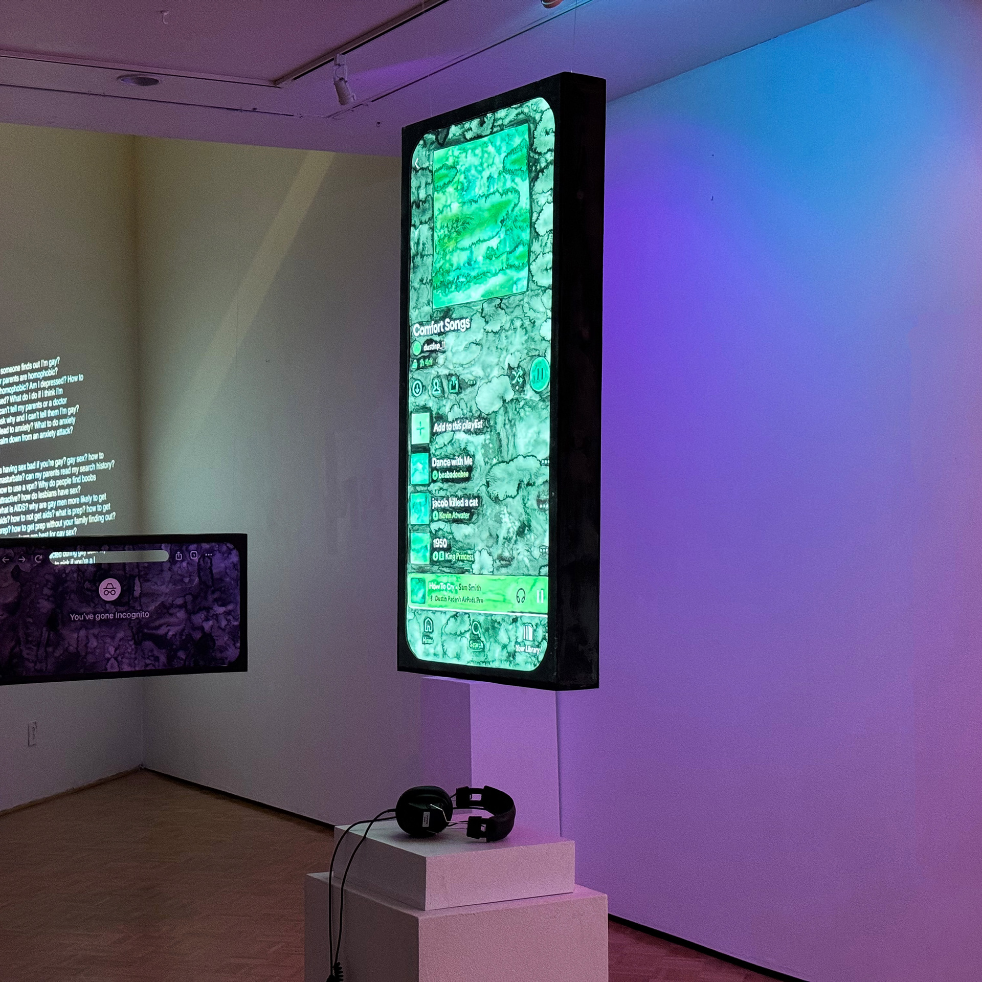 Spotify Shy installation image: green watercolor painting of private spotify playlist. The song titles are by queer artists. Under the hanging installation is a pedestal with headphones.