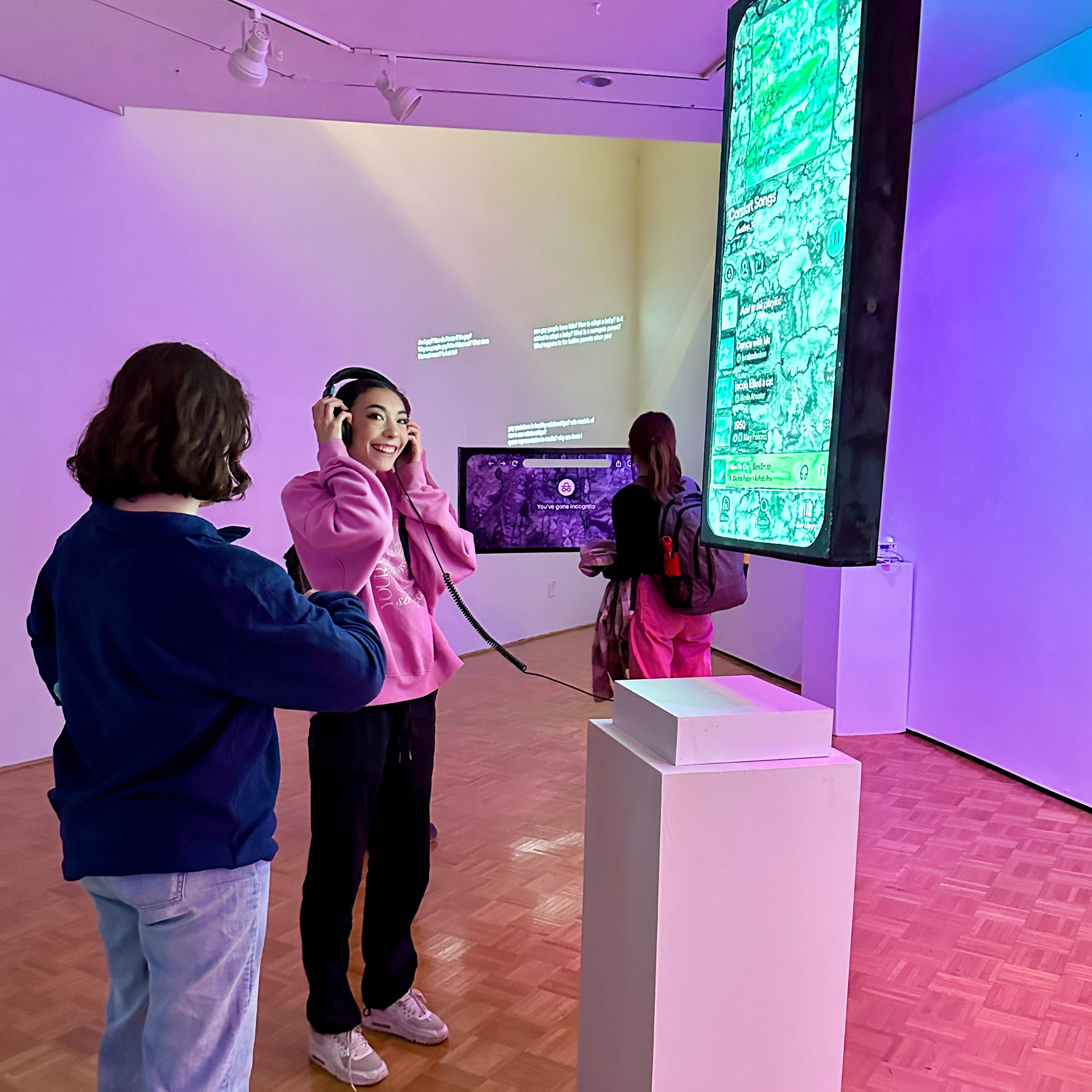 College student girl in pink sweater smiles while wearing the headphones, listening to the song and looking at the installation.