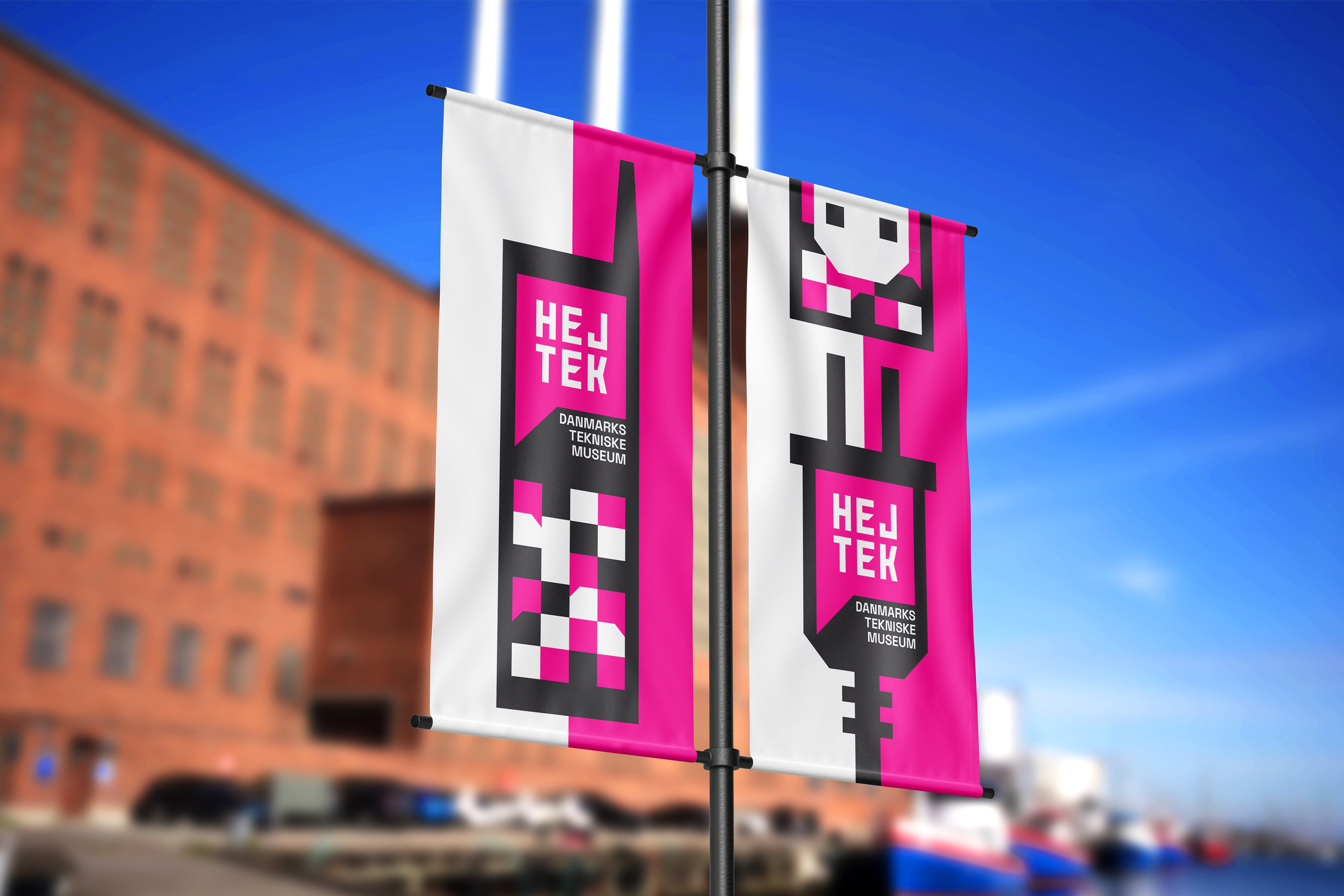 2 banners with pink, white, and black tech graphic elements advertising in front of the new brick building on a blue sky.