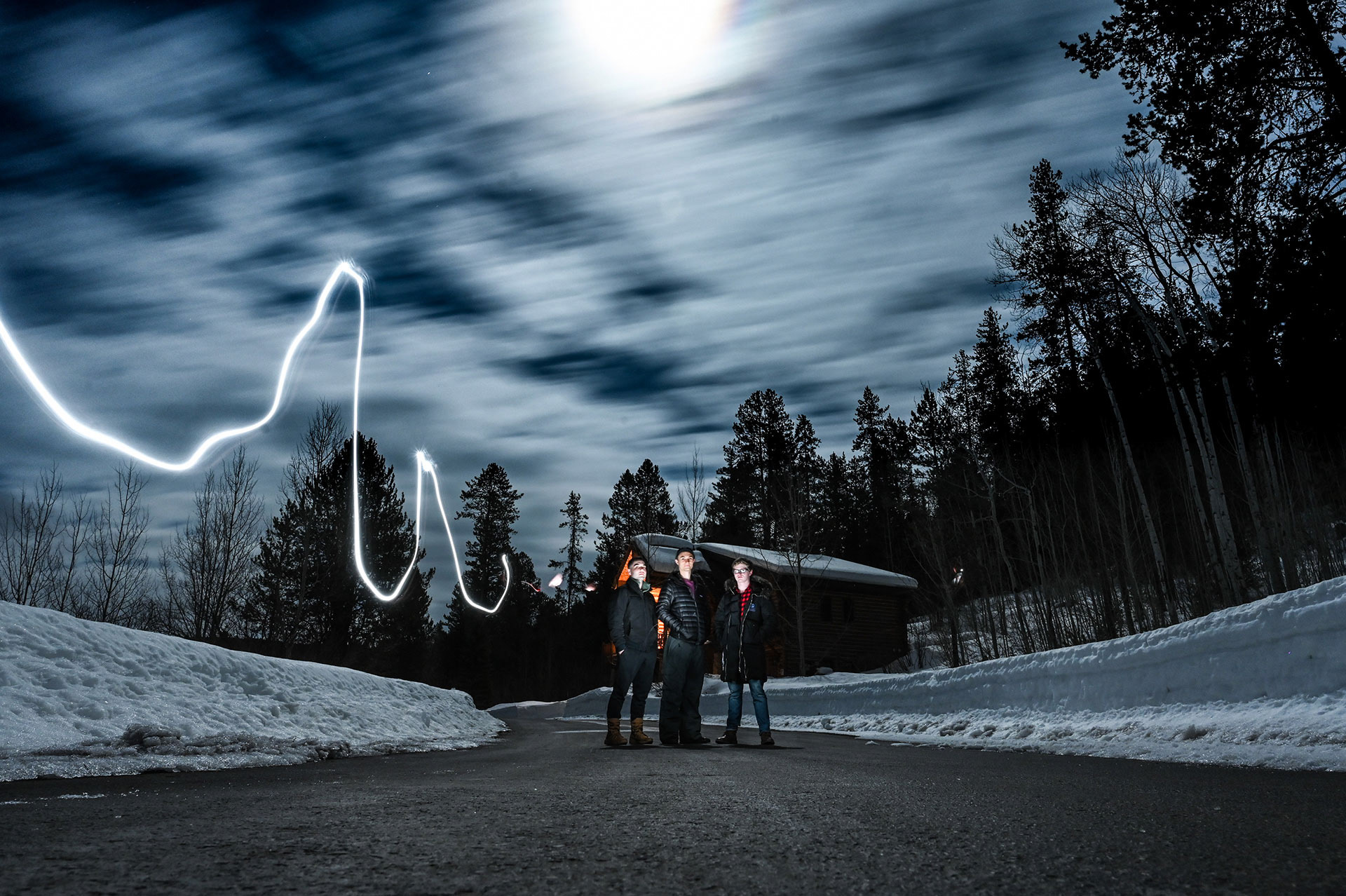 Three friends posing in the road with a line of light leading to them
