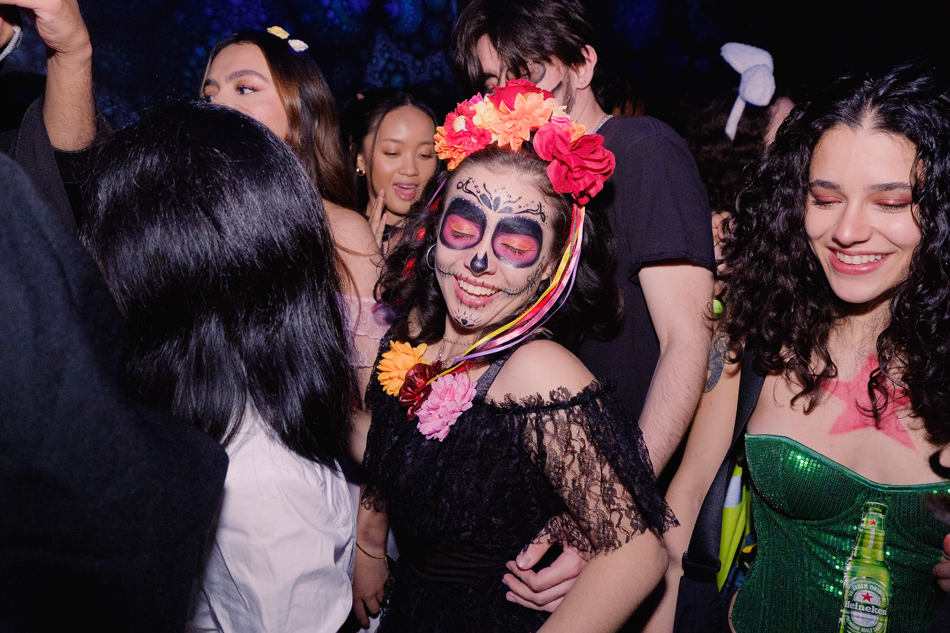 Guest with skull makeup smiling under red and purple lights at Toronto nightclub Halloween celebration